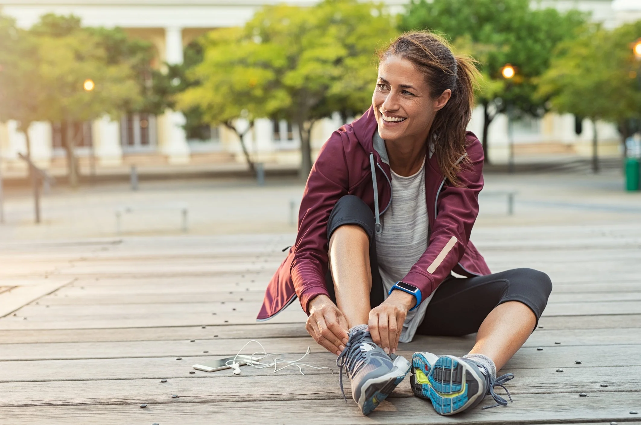 Woman in athletic clothing stretching on a wooden deck outdoors, with trees and buildings in the background.