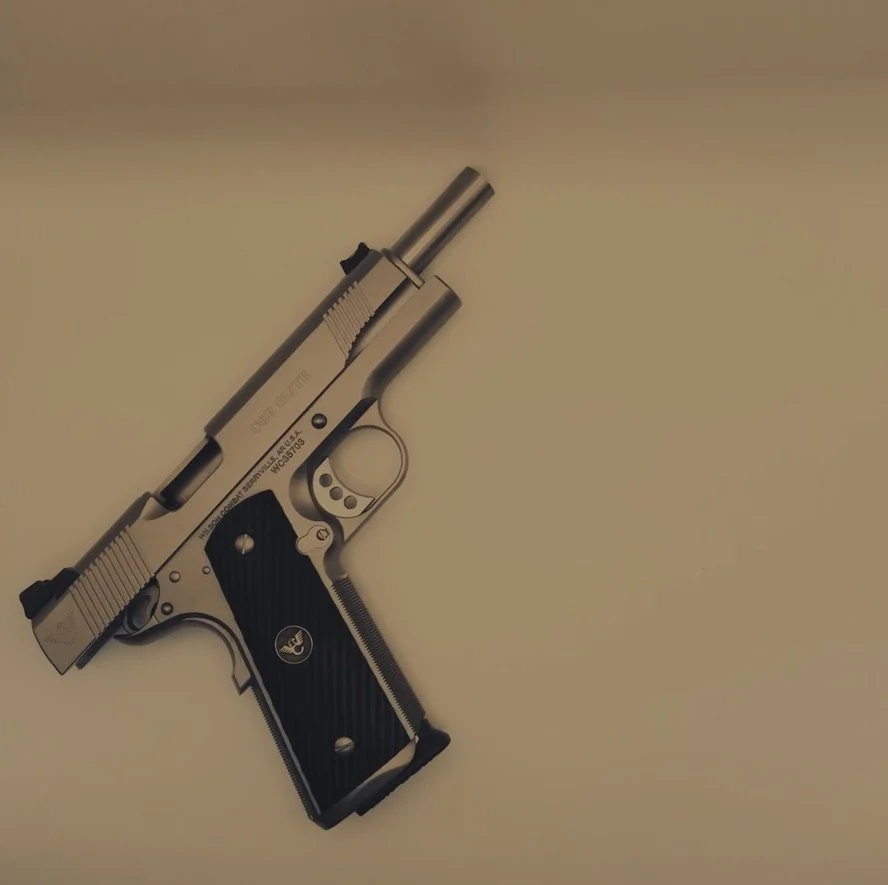 A stainless steal Wilson Combat CQB Elite with fiber optic sights and a custom trigger job laying on it's side with the slide locked back. The Wilson Combat Logo shows through cleanly against the black custom grips.