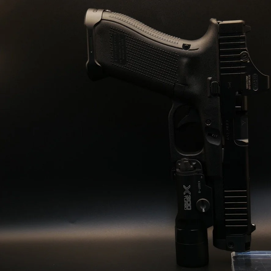 a Glock 45 with a Holosun SCS, Surefire X300 and a tryrant magazine well stands up muzzle down balanced on it's flashlight against a black background.