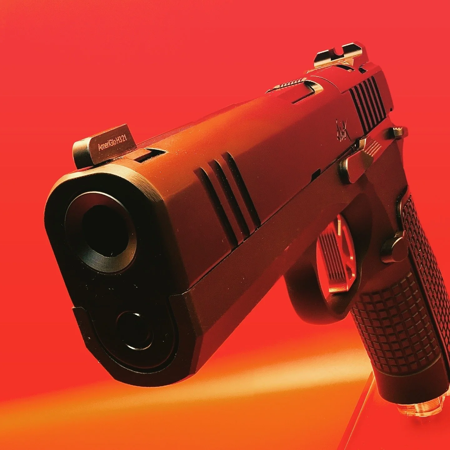 A black Dan Wesson DWX handgun with a textured grip and it's muzzle is held at an downward angle against a red background.
