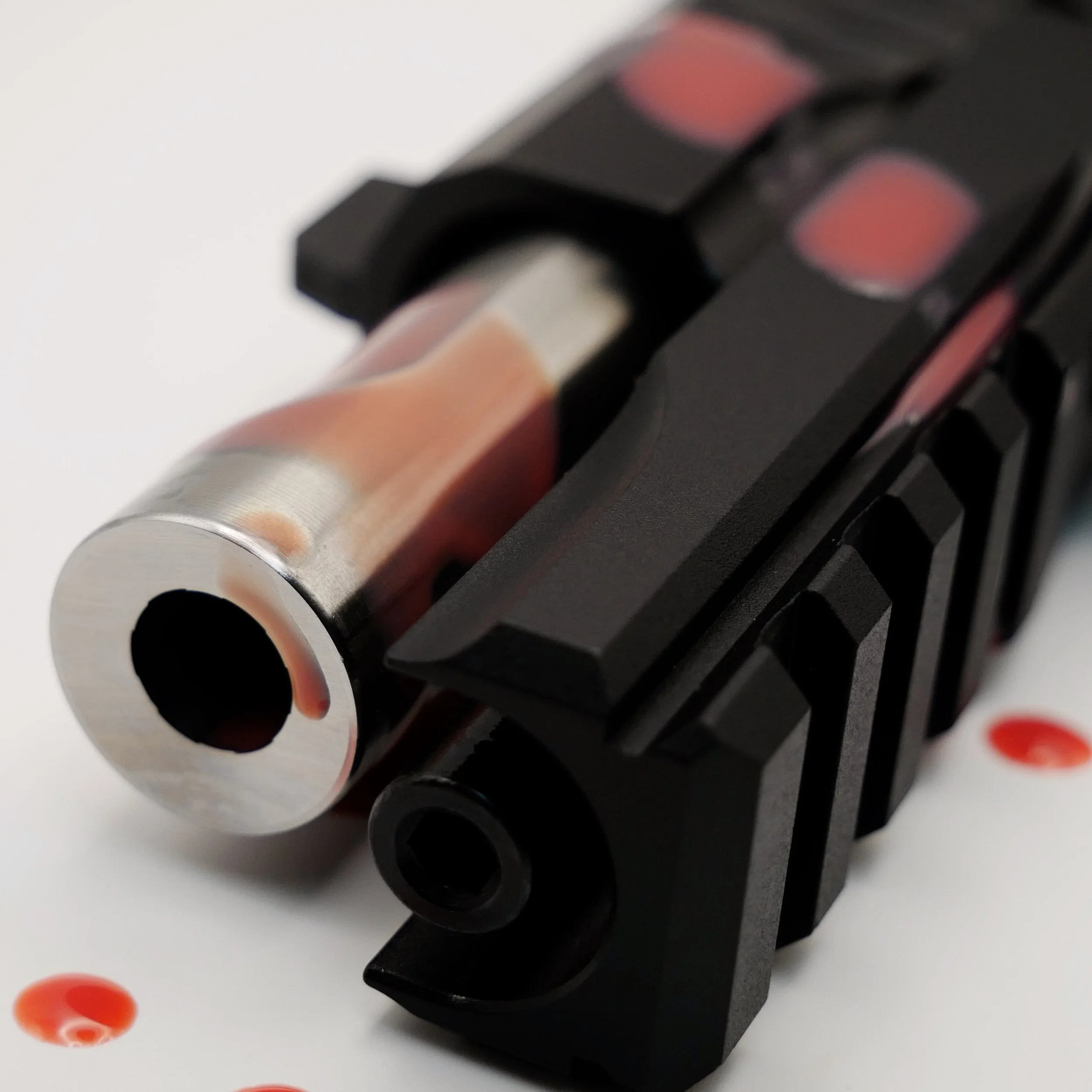 Close-up of an Jacob Grey ST9 black tactical handgun with pink accents, focusing on the barrel and slide, placed on a white surface with red dots.