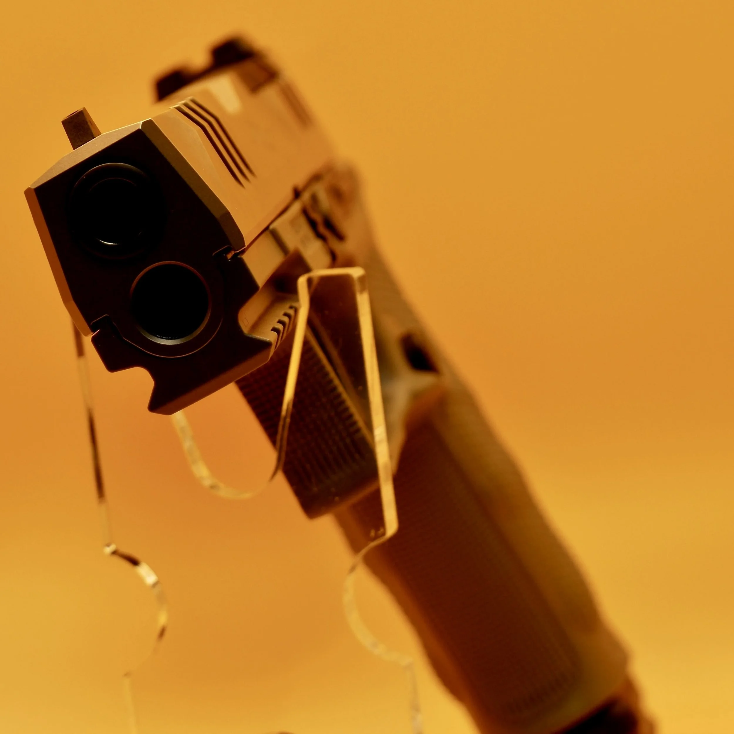 A semi-automatic Walther PDP with a tan frame and slide, pointed toward the camera, set against a yellow background with hanging spiral-shaped decorations.