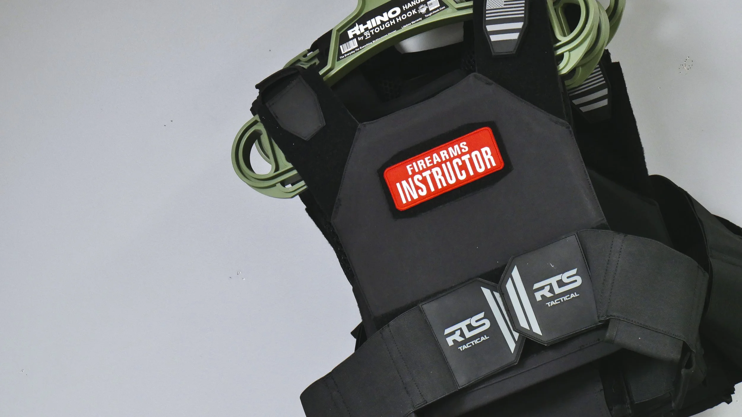 A few rts bullet proof vests hang from a rhino hangar on a wall within a classroom at an indoor shooting range.