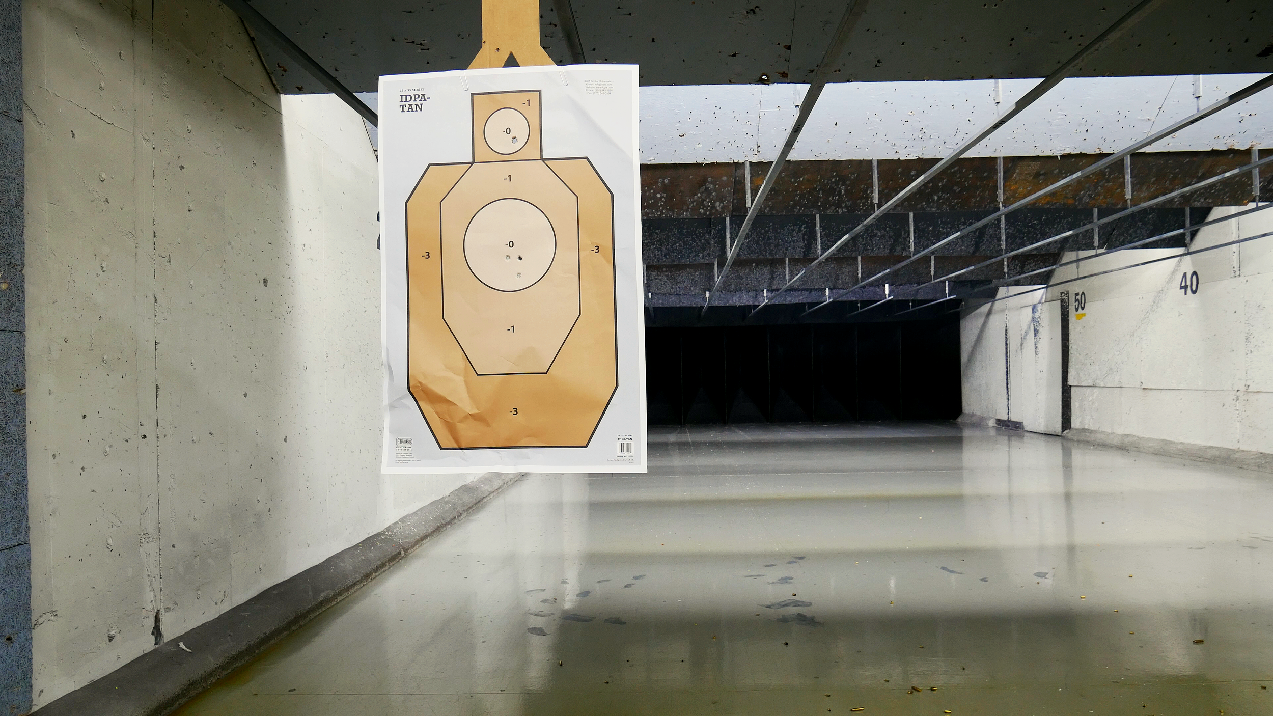An IDPA tan target hangs up at an indoor gun range in Washington. There are accurate shots placed in the a zone and the head.