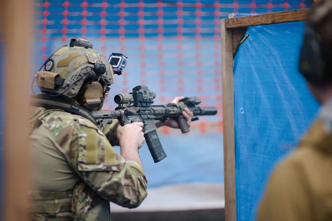 Citizen in camouflage gear aiming an suppressed ar15 rifle through a firing range barricade at a washington state rifle match.