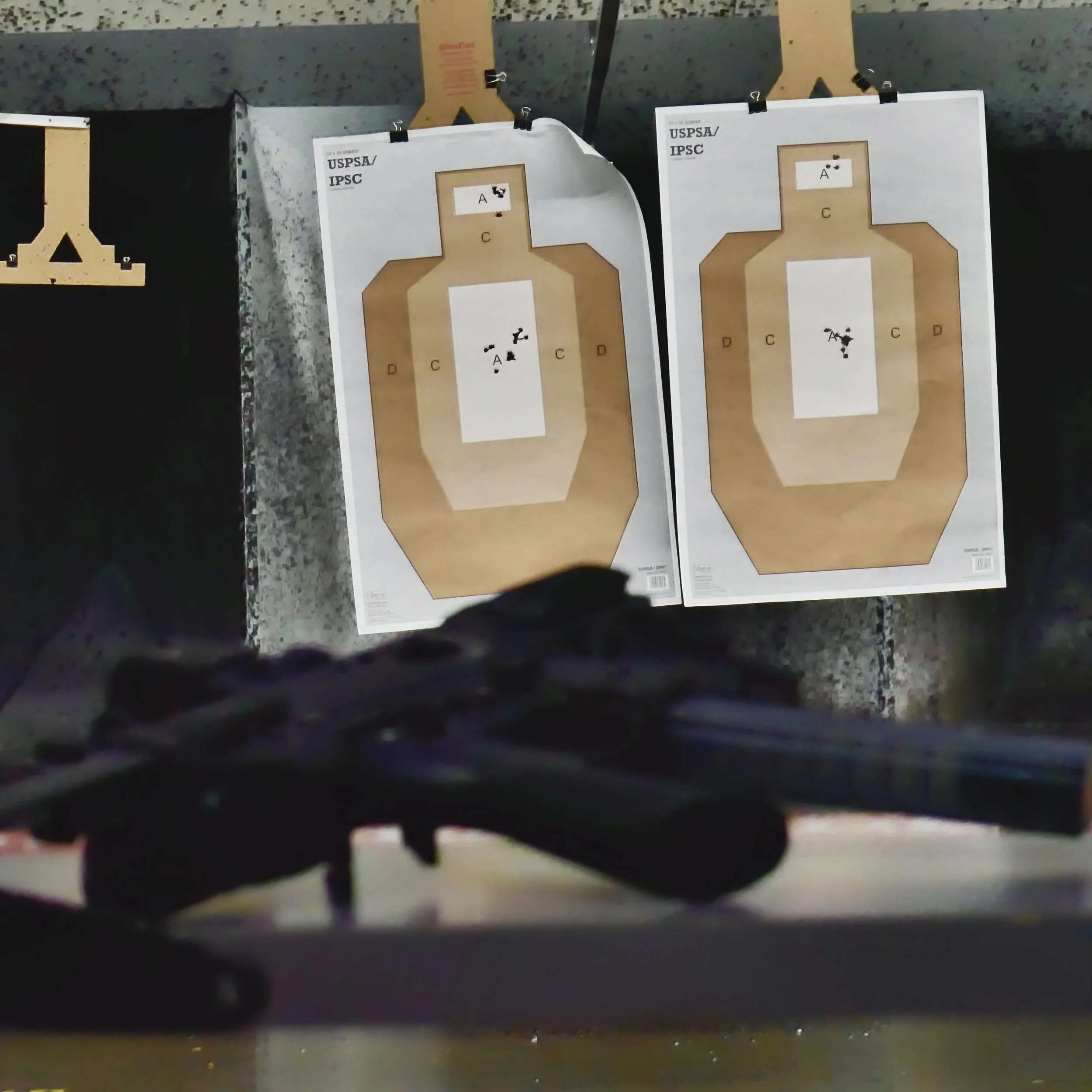 A B&T GHM9 SBR w/ an aimpoint macro lay on a shooting range table with two uspsa/ipsc targets hanging down range in front of the bullet traps..