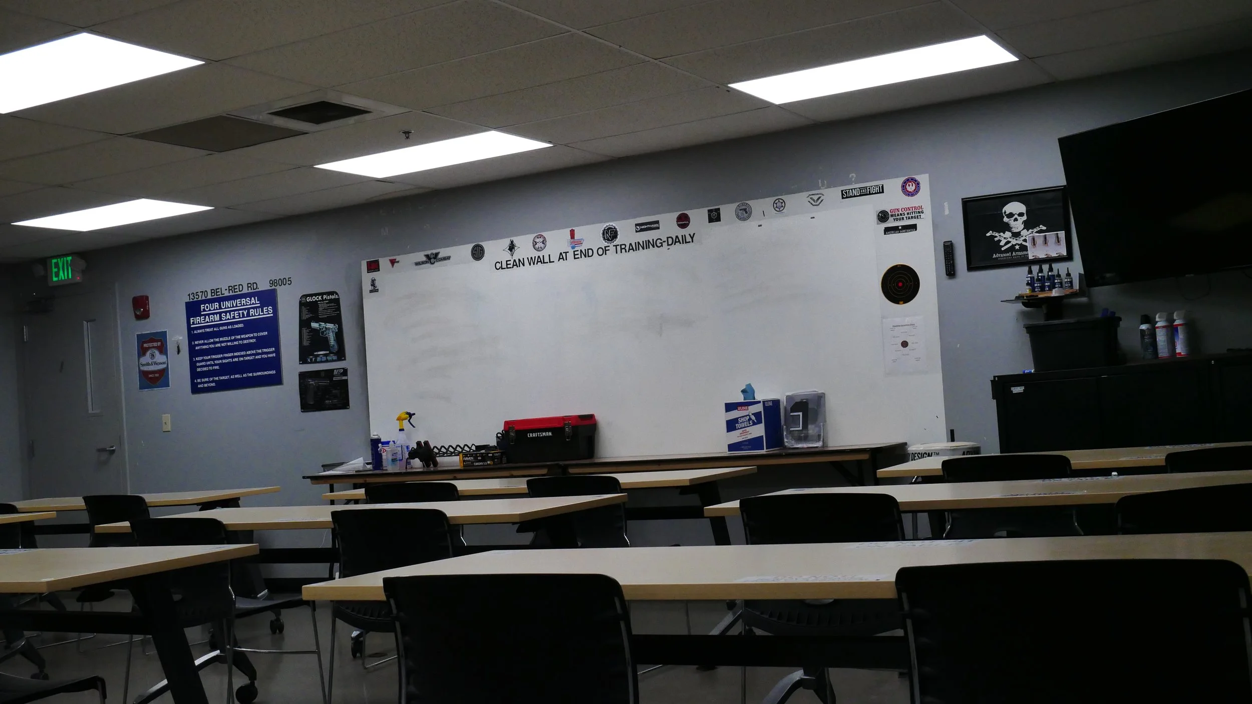 A shooting range classroom with a white board, tv, desks and chairs is prepped for class.