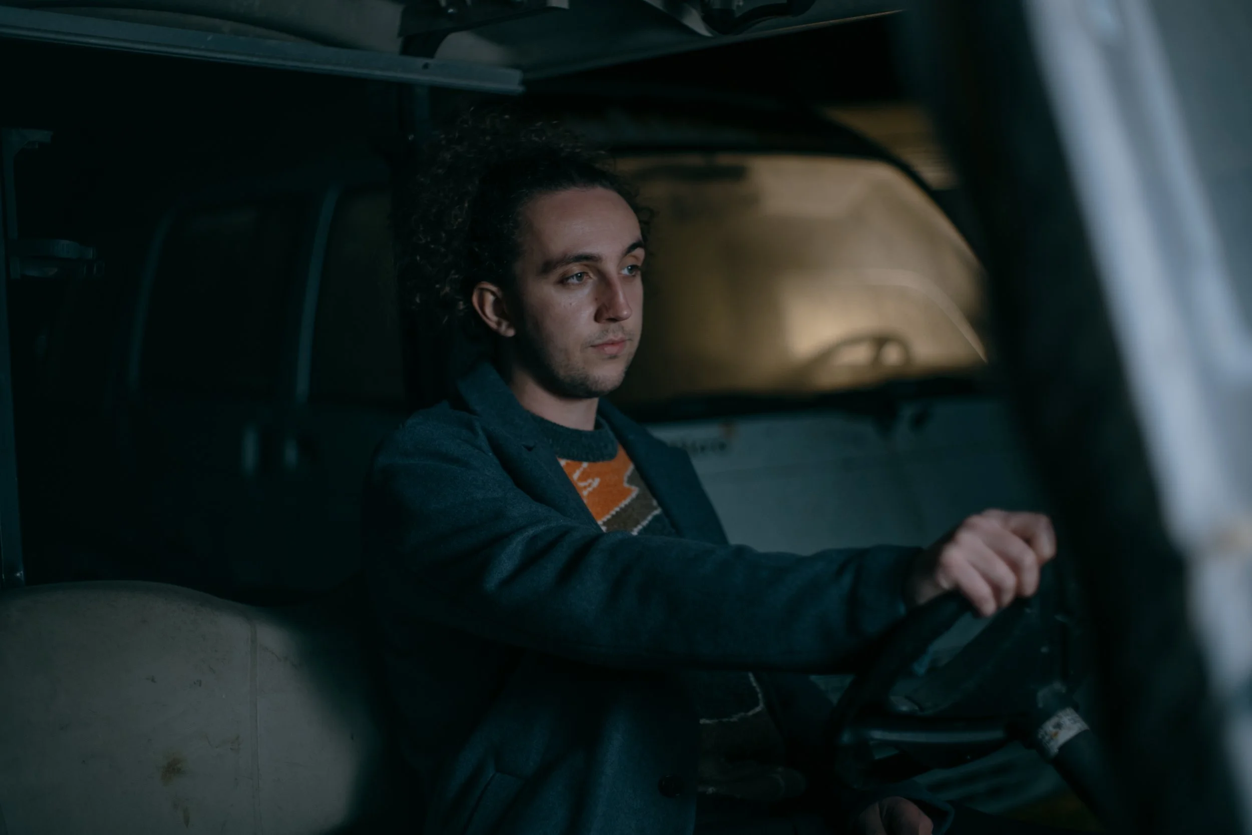 A young man with curly hair sitting in the driver's seat of a vehicle, looking serious and focused. Photo by Vincent Prograce