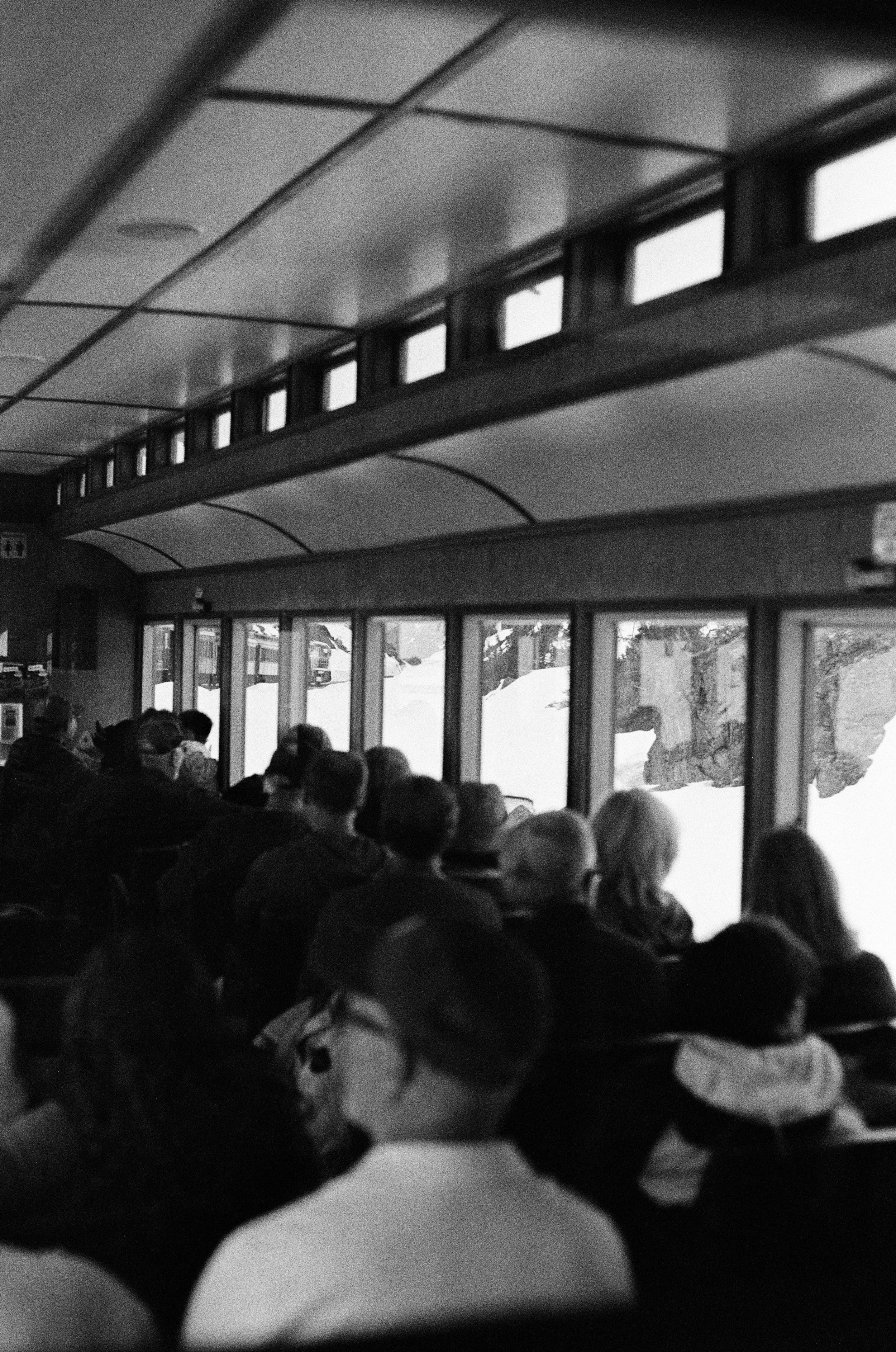 People seated inside a bus or train, looking out the windows at snowy landscape with rocks and trees. Photo by Vincent Prograce