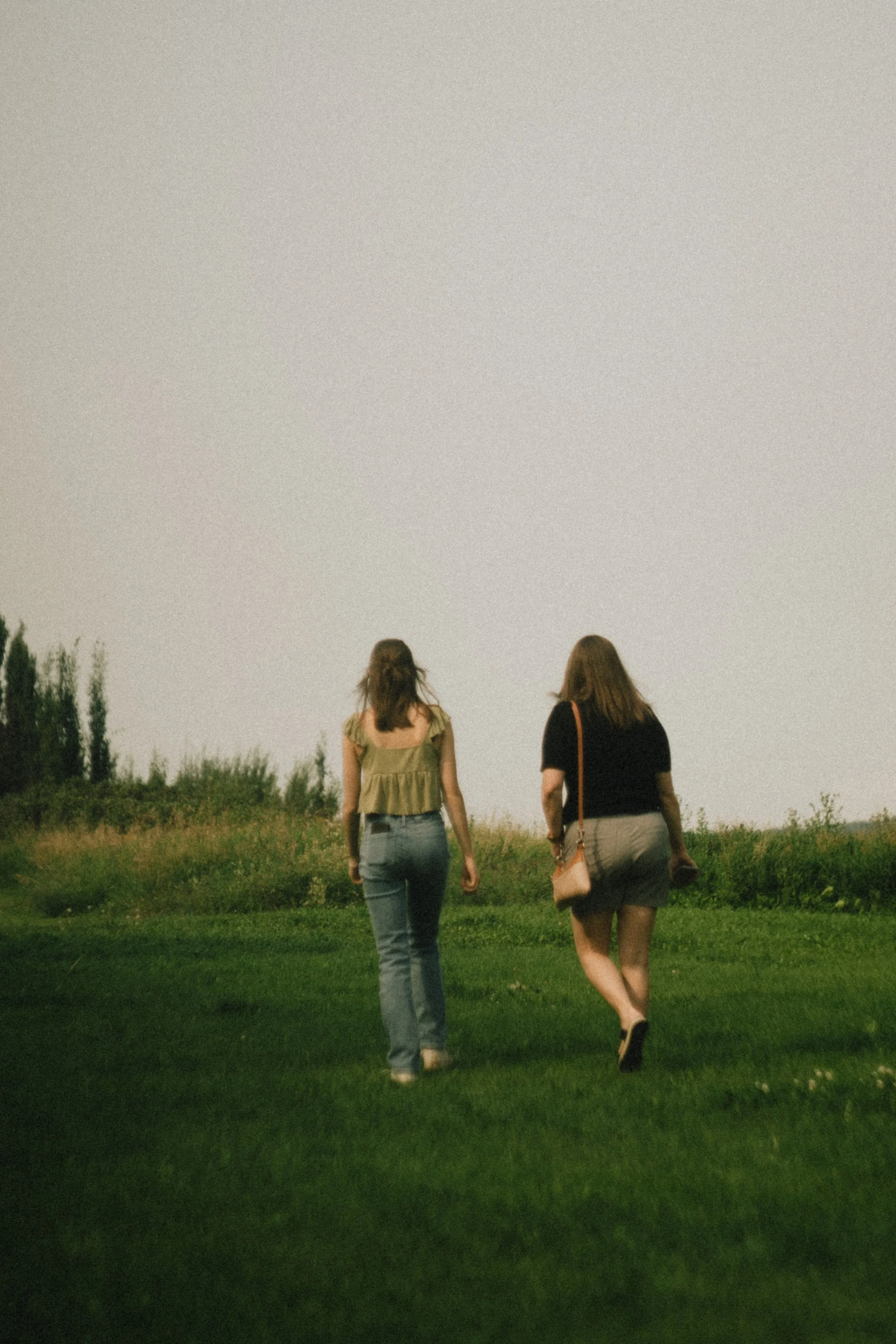 Two women walking on a grassy field, seen from behind, with an open sky above. Photo by Vincent Prograce