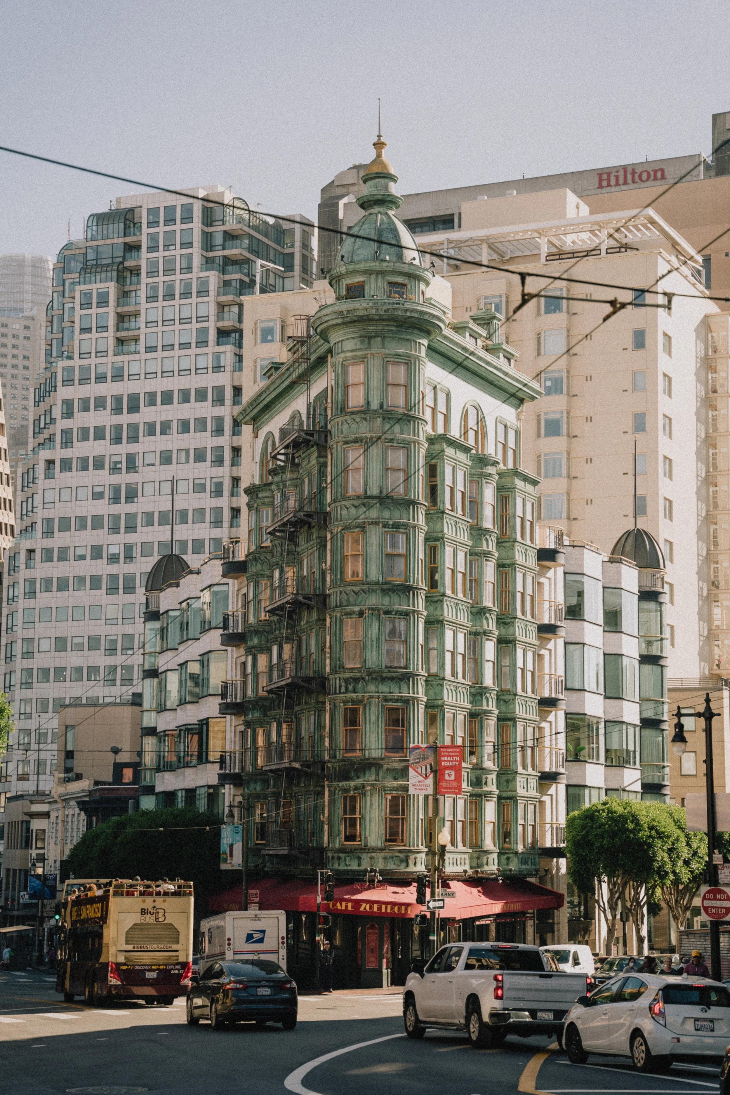 A historic green Victorian-style building on a busy city street in San Francisco, California, with modern high-rise buildings in the background. Photo by Vincent Prograce