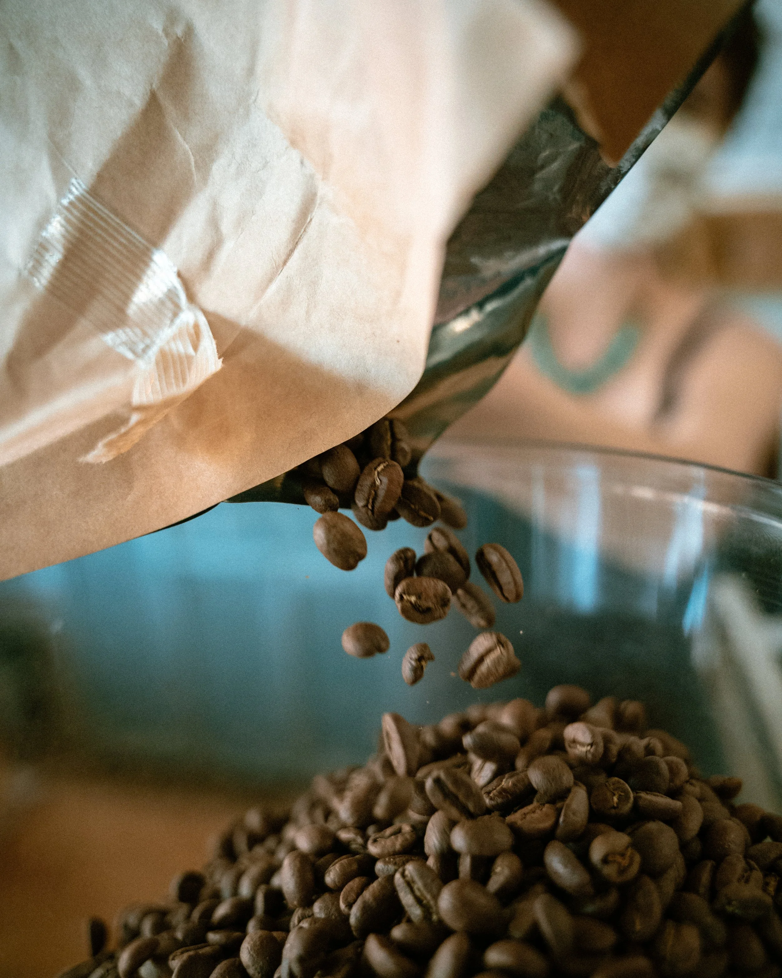 Coffee beans spilling from a brown paper bag into a glass container. Photo by Vincent Prograce
