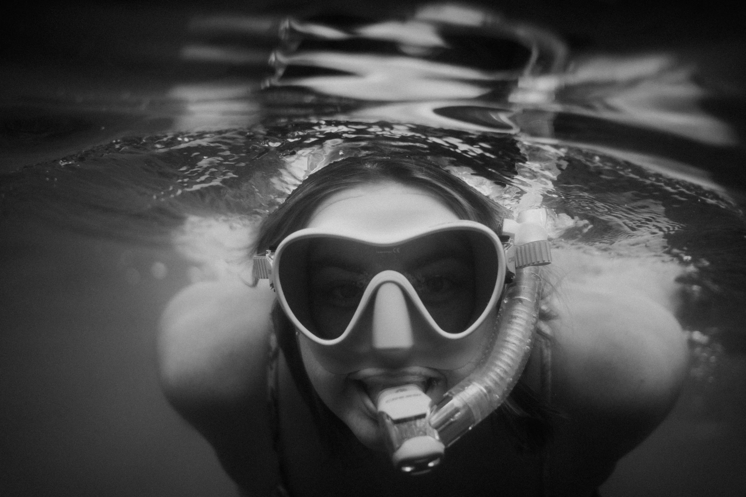 A person in ocean wearing goggles and a snorkel, with their face partially submerged in water. Photo by Vincent Prograce