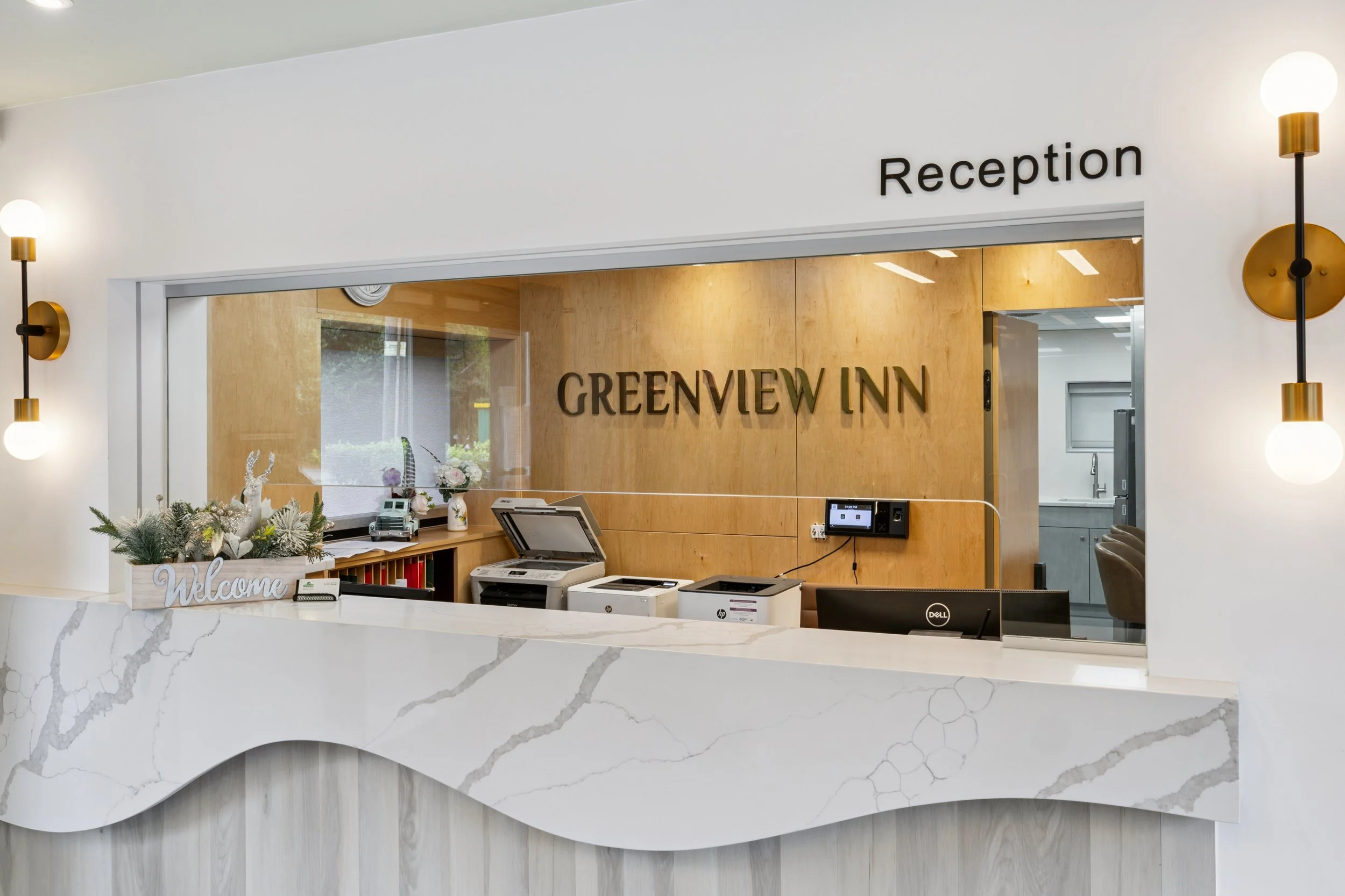 Reception desk area of GreenvieW Inn hotel with a marble counter, decorations, and a wooden wall sign.