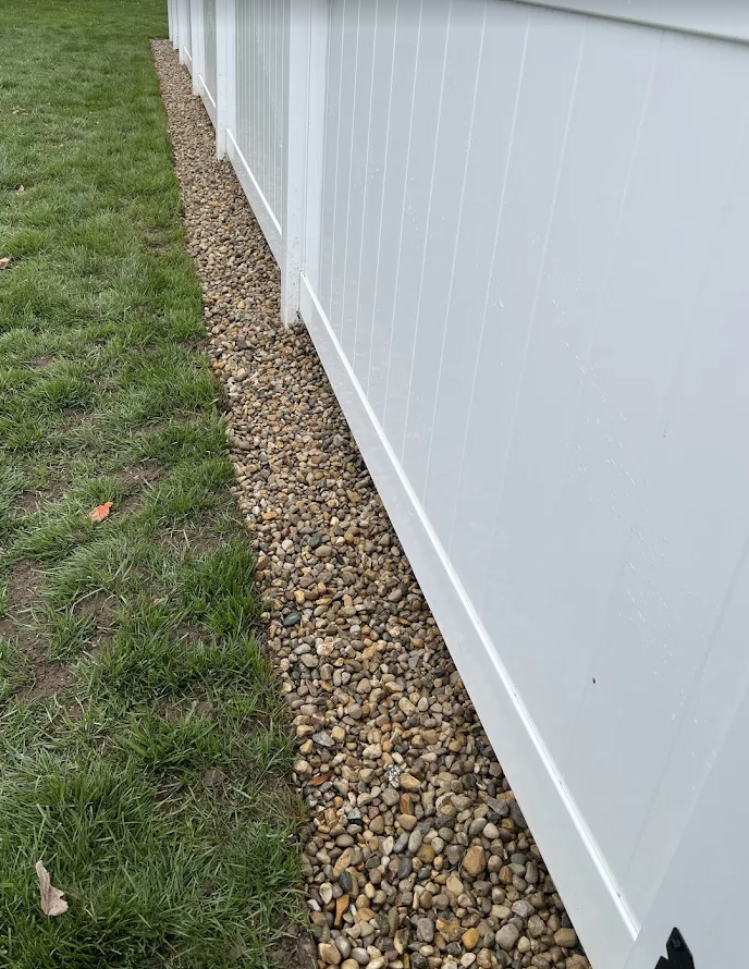 Gravel Foundation along the side of a white fence with grass on the opposite side.