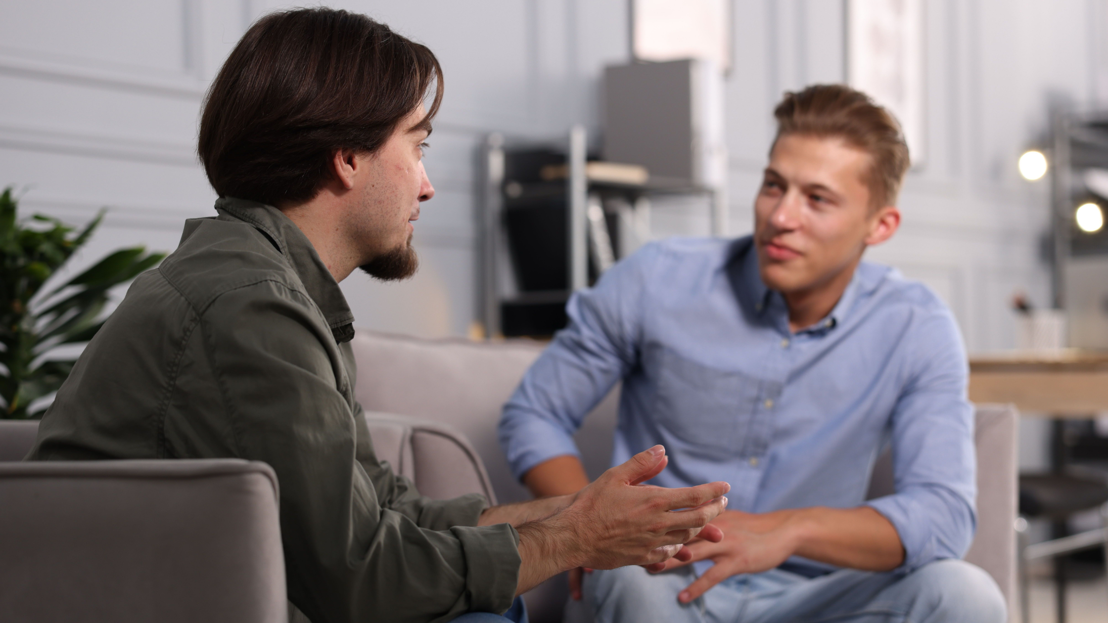 Two colleagues sitting on a couch in an office having an open, honest conversation about a difficult topic at work
