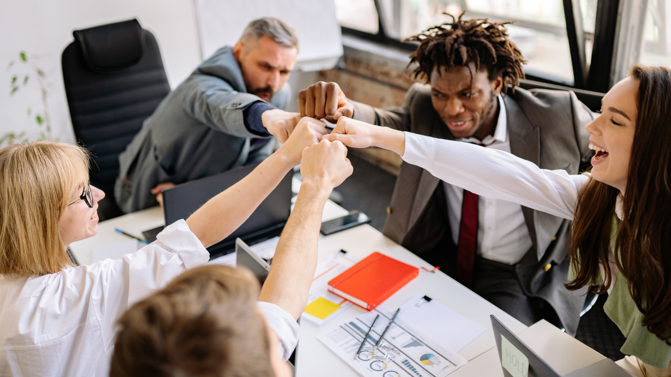 Team of colleagues celebrating with a group fist bump during a meeting, showing trust and connection in the workplace