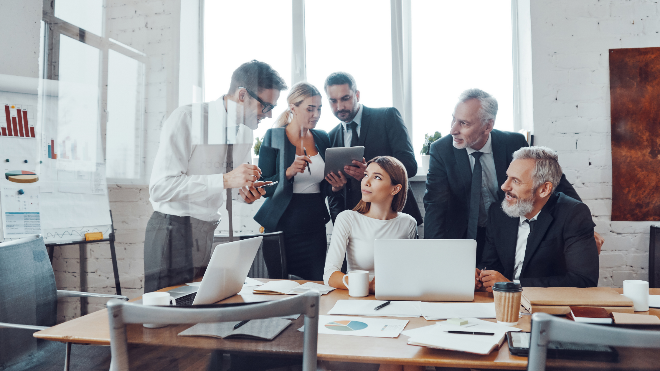 Leadership team gathered around a conference table with laptops and a tablet, collaborating in a modern office with large windows