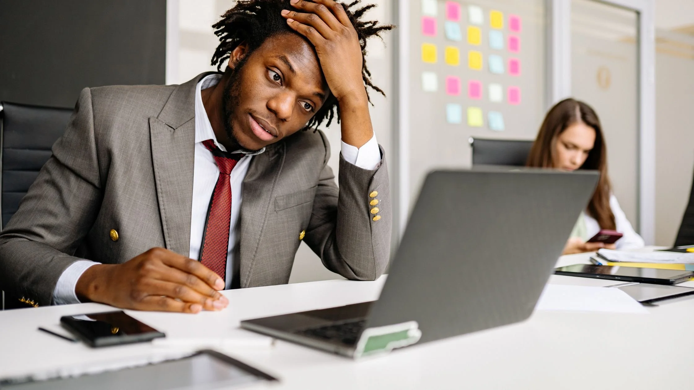 Tired office worker holding head while reviewing papers beside a laptop