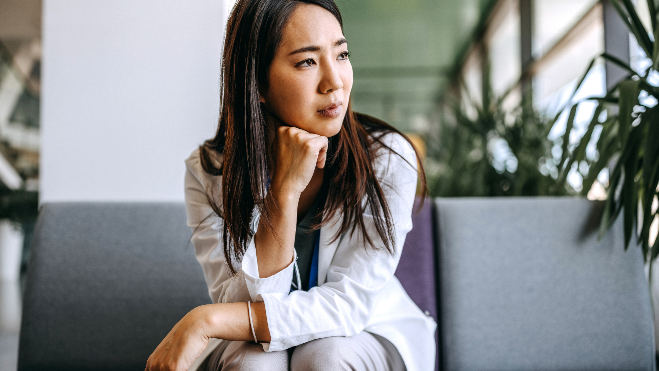 Professional woman in a dark blazer holding her head in both hands at her desk, visibly overwhelmed — illustrating the emotional toll of workplace burnout