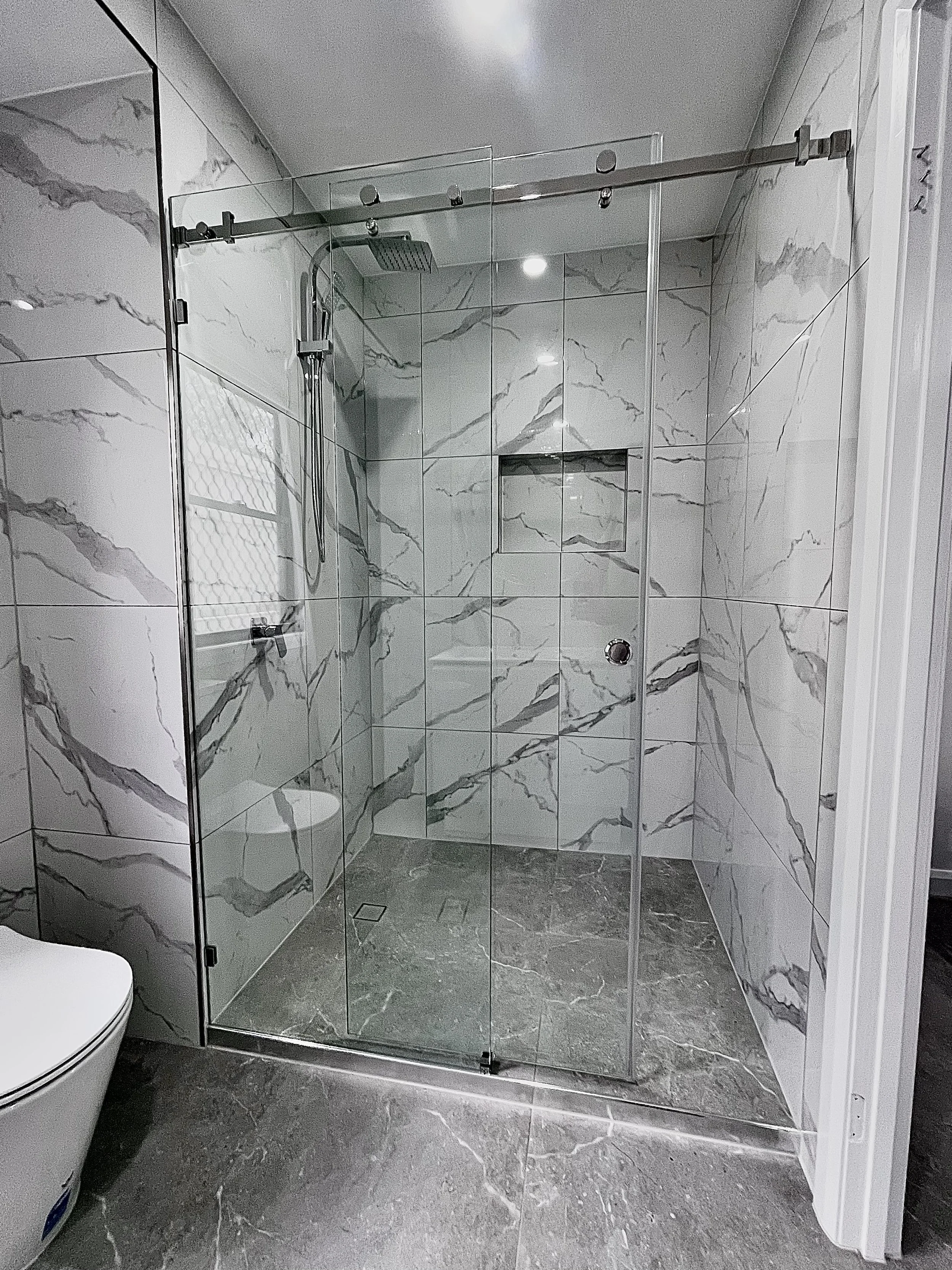 Modern walk-in shower with glass sliding door, marble wall tiles, a built-in niche, and a rain shower head
