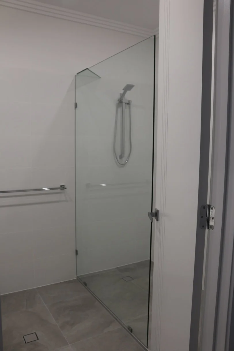 Glass shower enclosure with a handheld shower head, a towel bar on the wall, and tiled floor.
