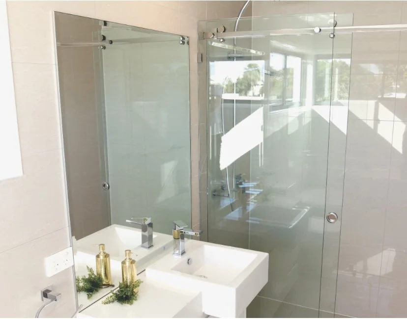Modern bathroom with a white sink, soap dispenser, small plants, a large mirror, and a glass-enclosed shower area.