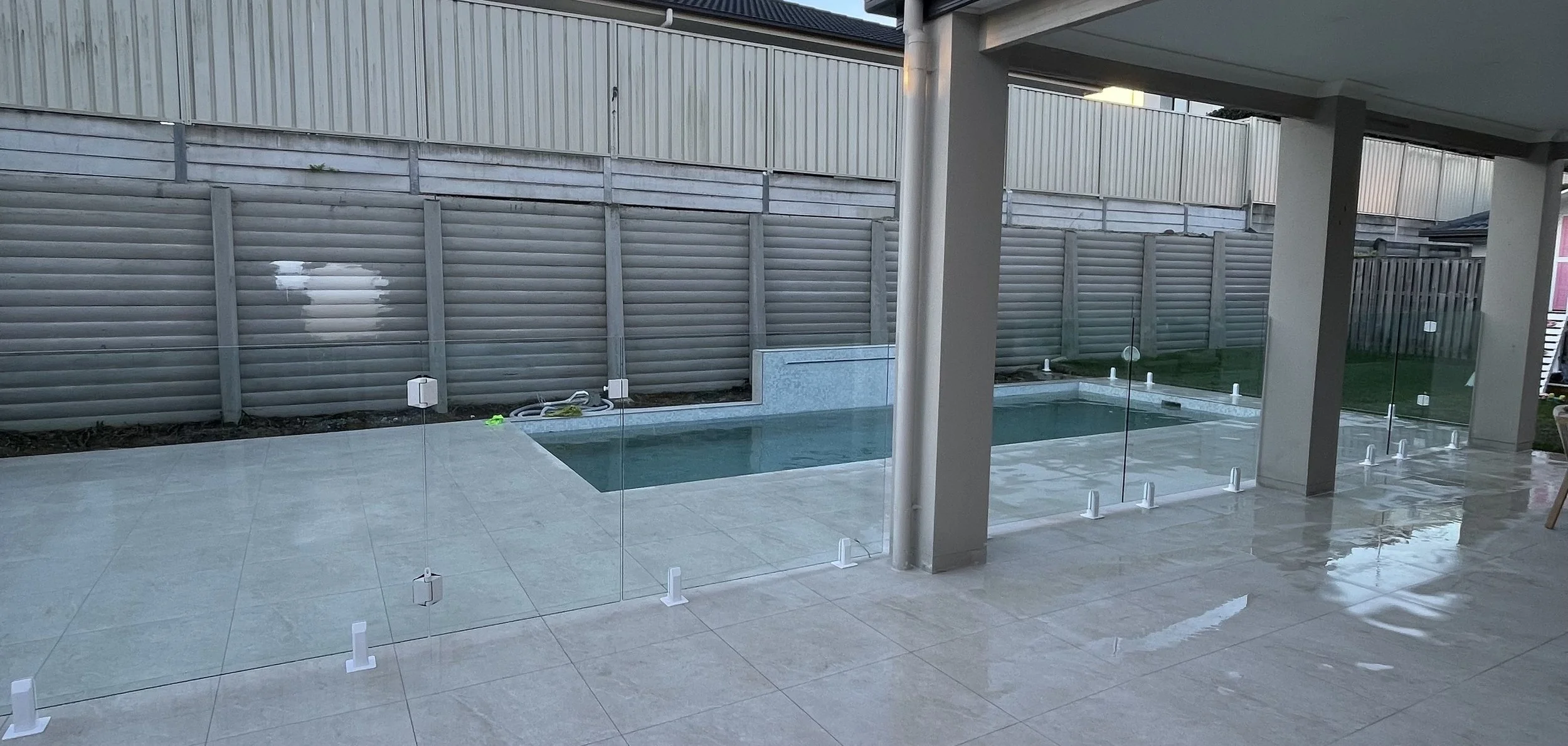 Partially enclosed backyard with small swimming pool, glass fencing, concrete patio, and grey privacy fence