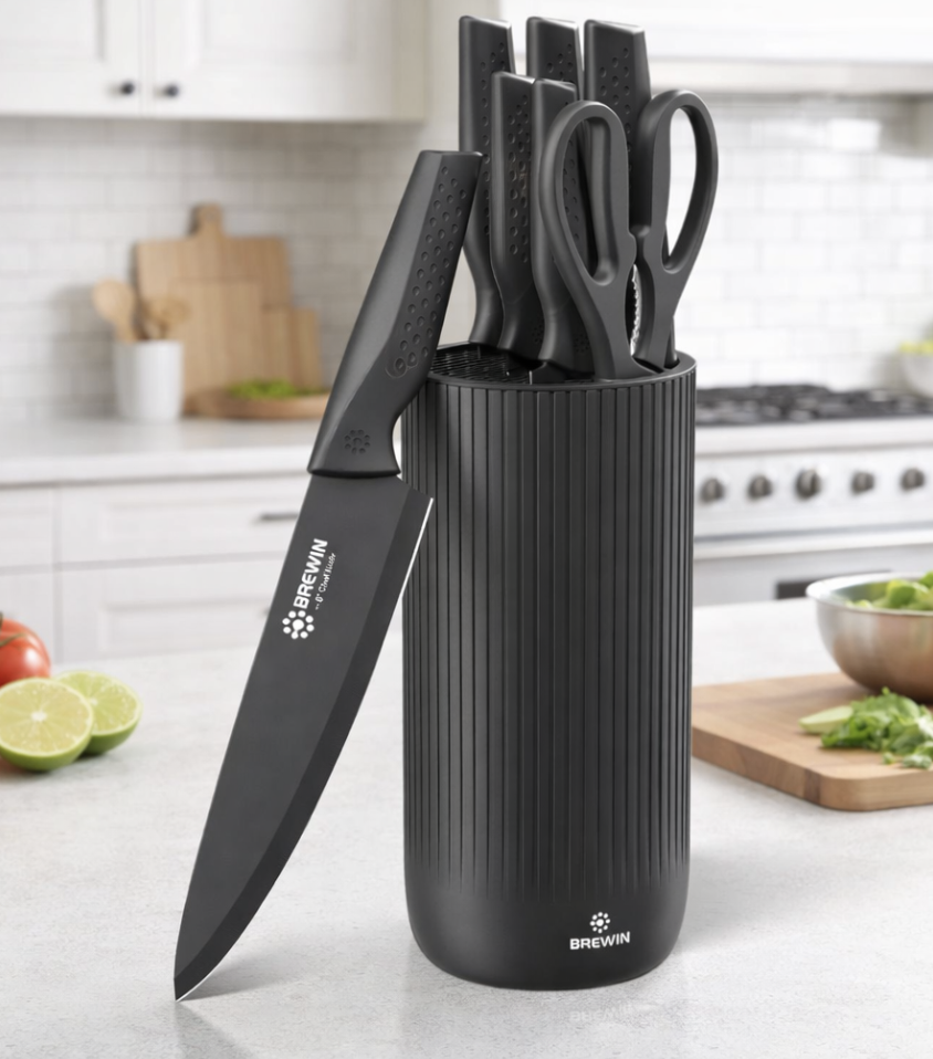 A set of four black kitchen knives and a pair of scissors stored in a cylindrical black knife holder on a kitchen countertop.