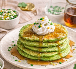 Stack of fluffy green pancakes topped with whipped cream, sprinkles, and maple syrup for a fun St. Patrick’s Day breakfast idea.