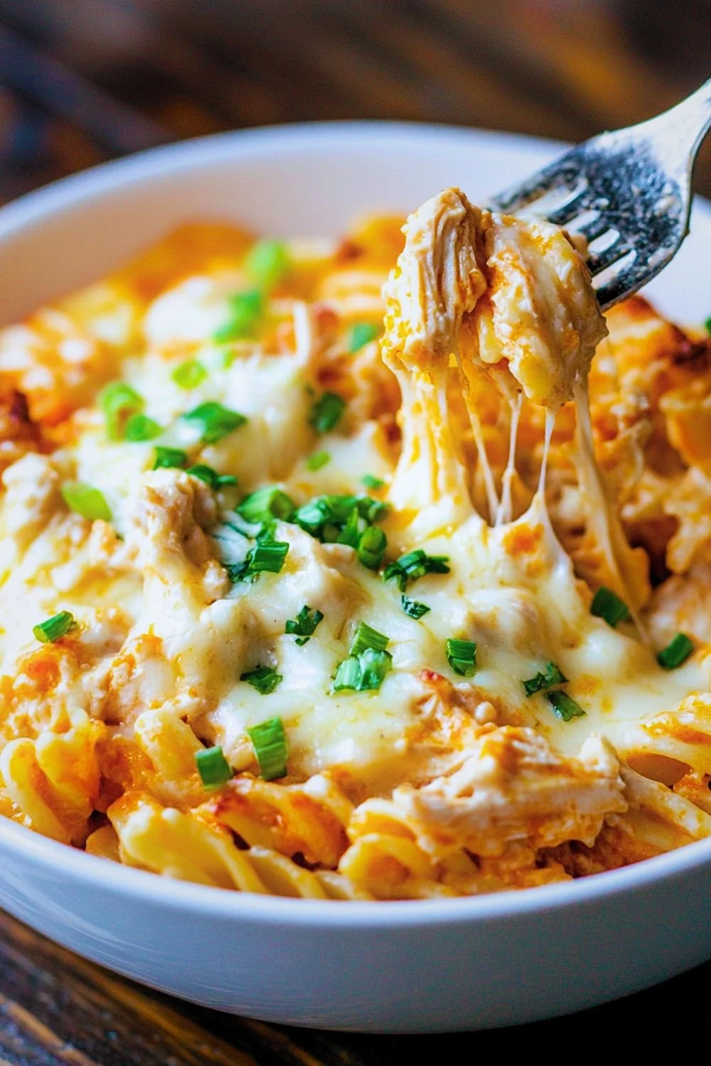 Spoonful of creamy baked buffalo chicken pasta pulled from casserole dish showing golden cheese crust and creamy buffalo ranch sauce
