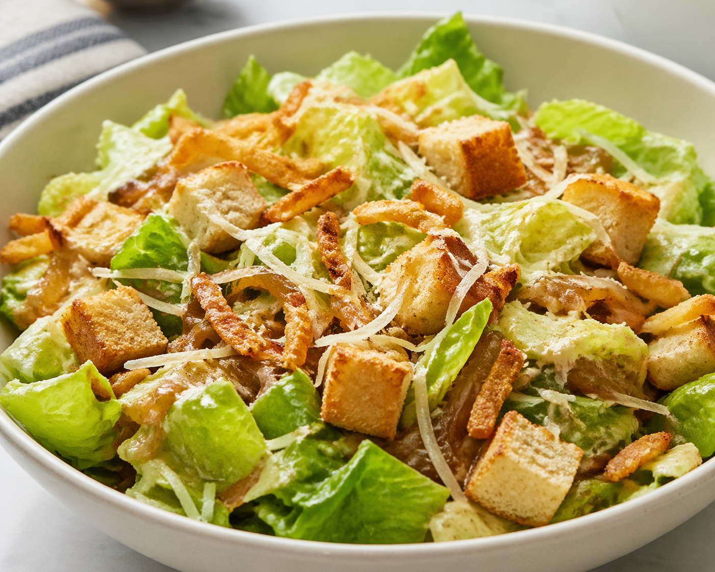 French onion crunch salad with romaine lettuce, crispy fried onions, shredded cheese, croutons, and creamy dressing in a white bowl