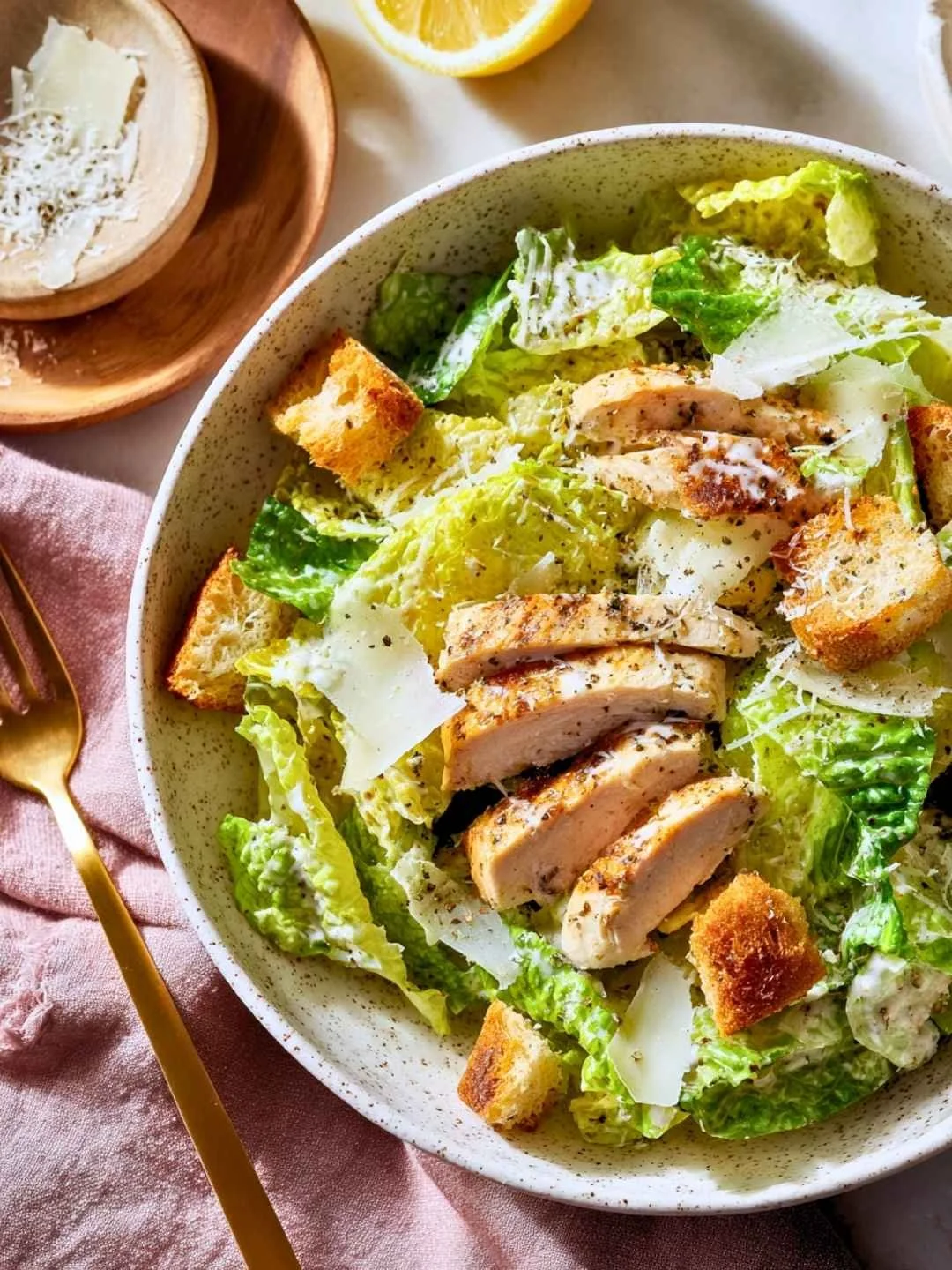 Chicken Caesar salad with grilled chicken, romaine, parmesan, and croutons in a speckled ceramic bowl.