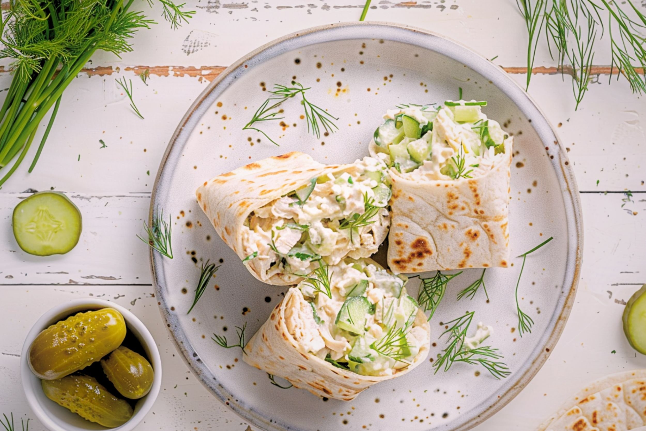 Dill pickle chicken salad wraps cut in half on a white plate showing creamy chicken salad filling with dill and pickles