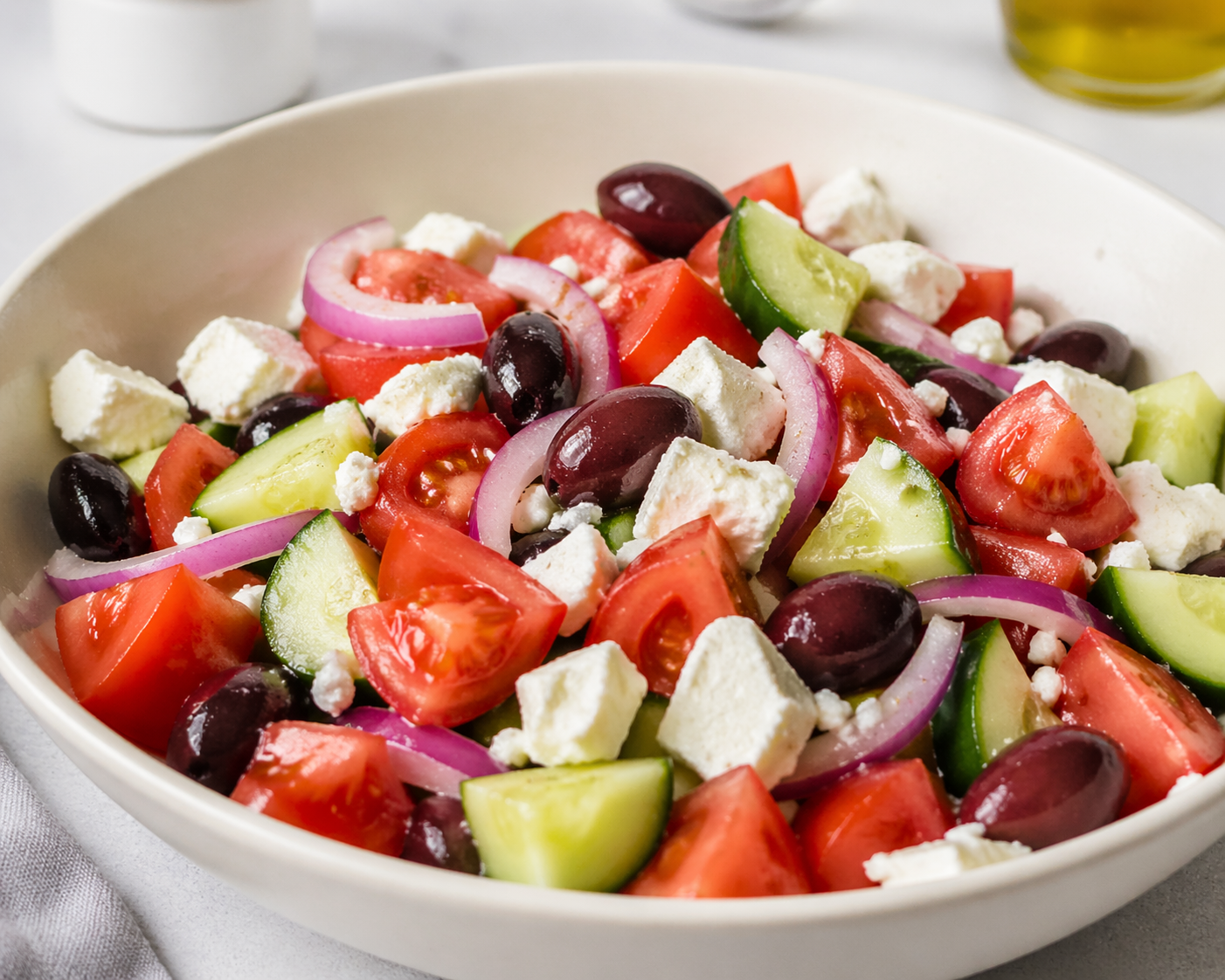 Fresh Greek salad with cucumber, tomatoes, feta cheese, kalamata olives, and red onion in a ceramic bowl with olive oil dressing