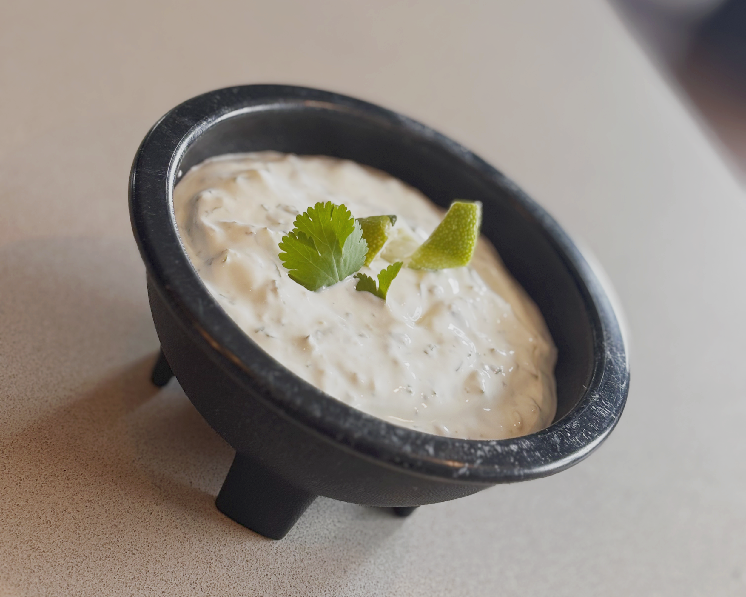Creamy cilantro lime crema in a small black bowl, garnished with fresh cilantro and lime, perfect for tacos, quesadillas, and bowls.