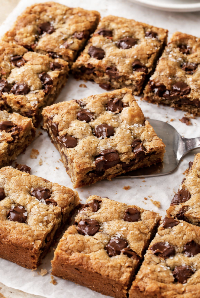 Gooey sourdough discard chocolate chip cookie bars cut into squares with melted chocolate chips and golden edges on parchment paper
