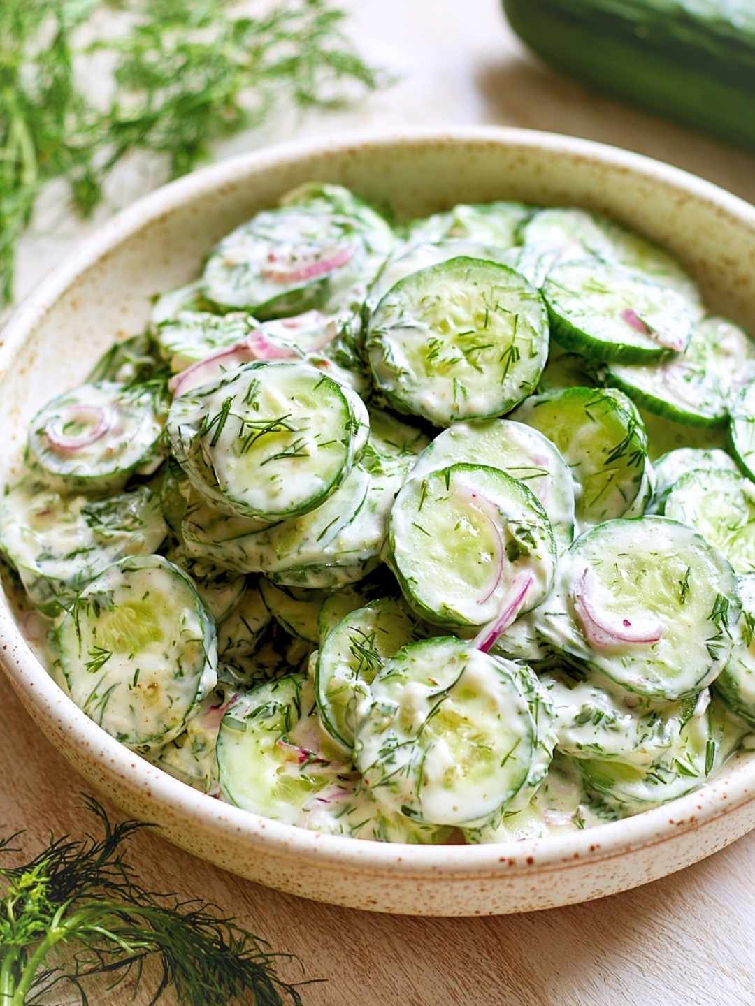 Creamy cucumber salad with fresh dill and red onion in a sour cream dressing in a speckled ceramic bowl.