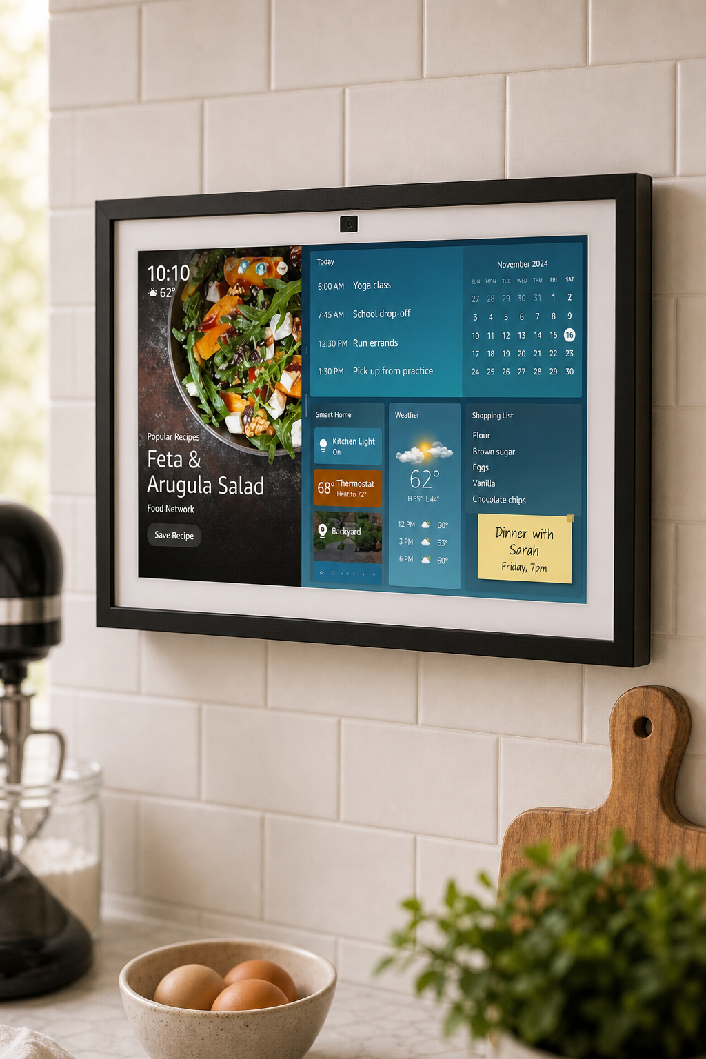 Echo Show 15-style smart display mounted on a white subway tile kitchen backsplash above a marble counter with warm natural light.