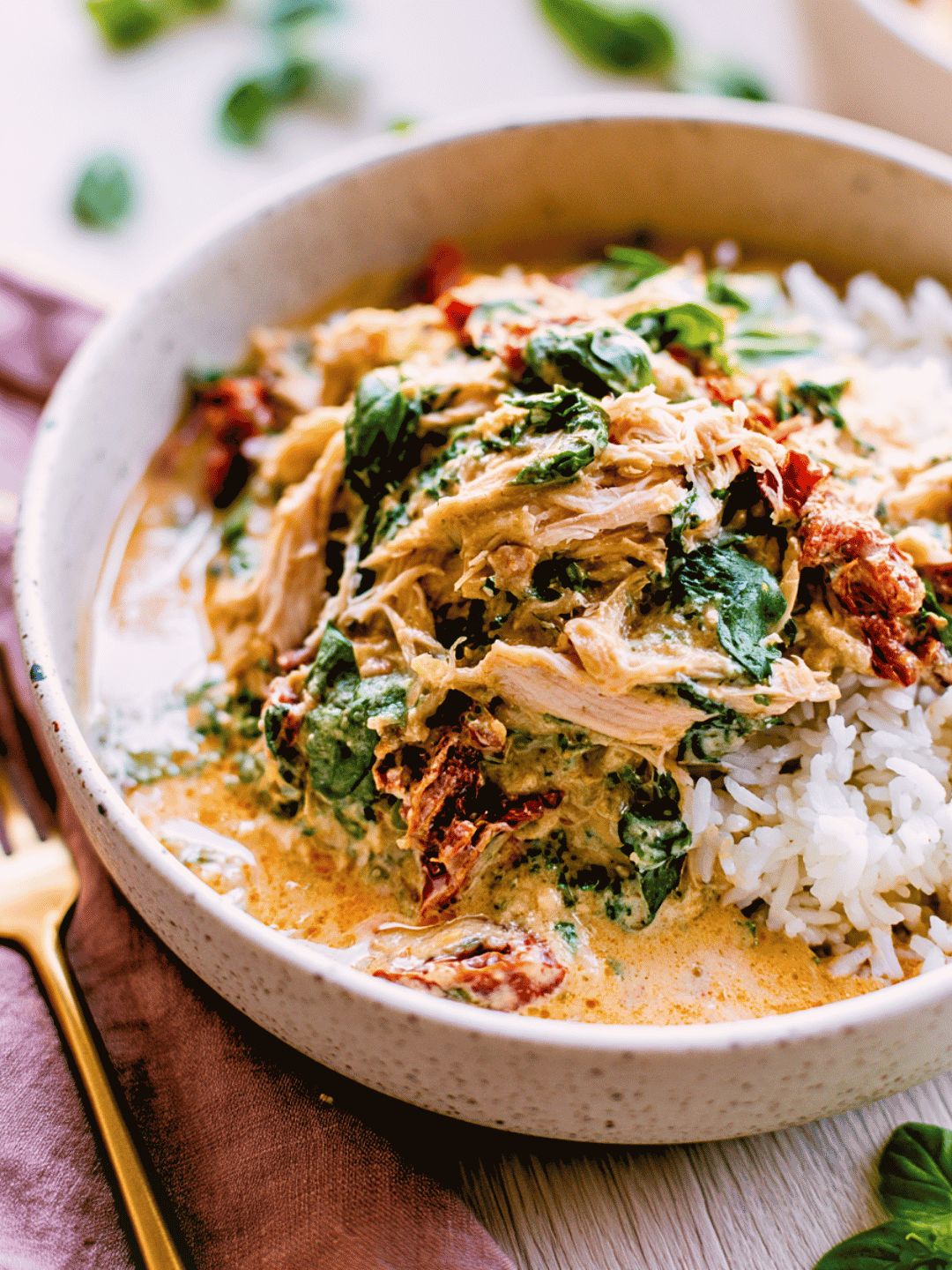 Creamy crockpot marry me chicken shredded over white rice with sun-dried tomatoes and spinach in a cream speckled bowl
