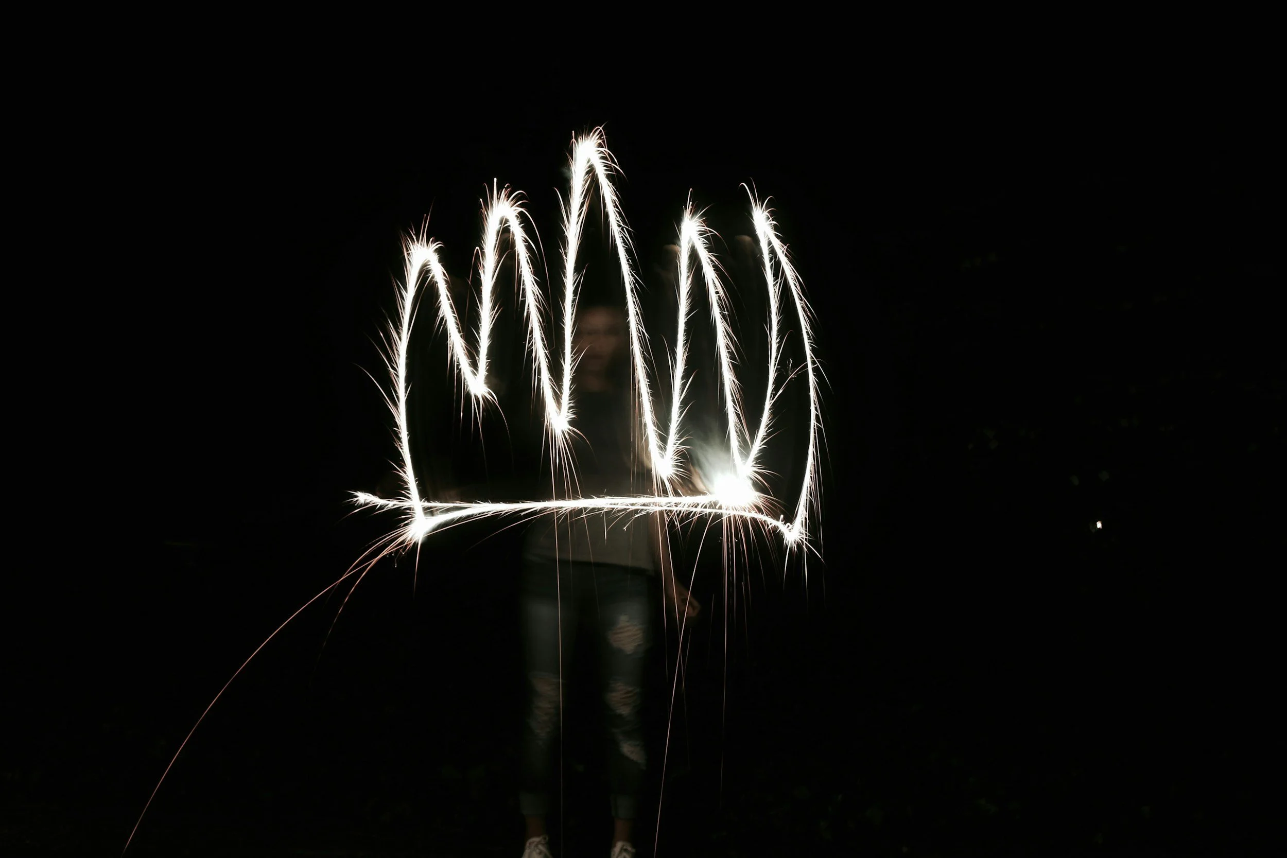 Person writing the word "LOVE" with sparklers at night.