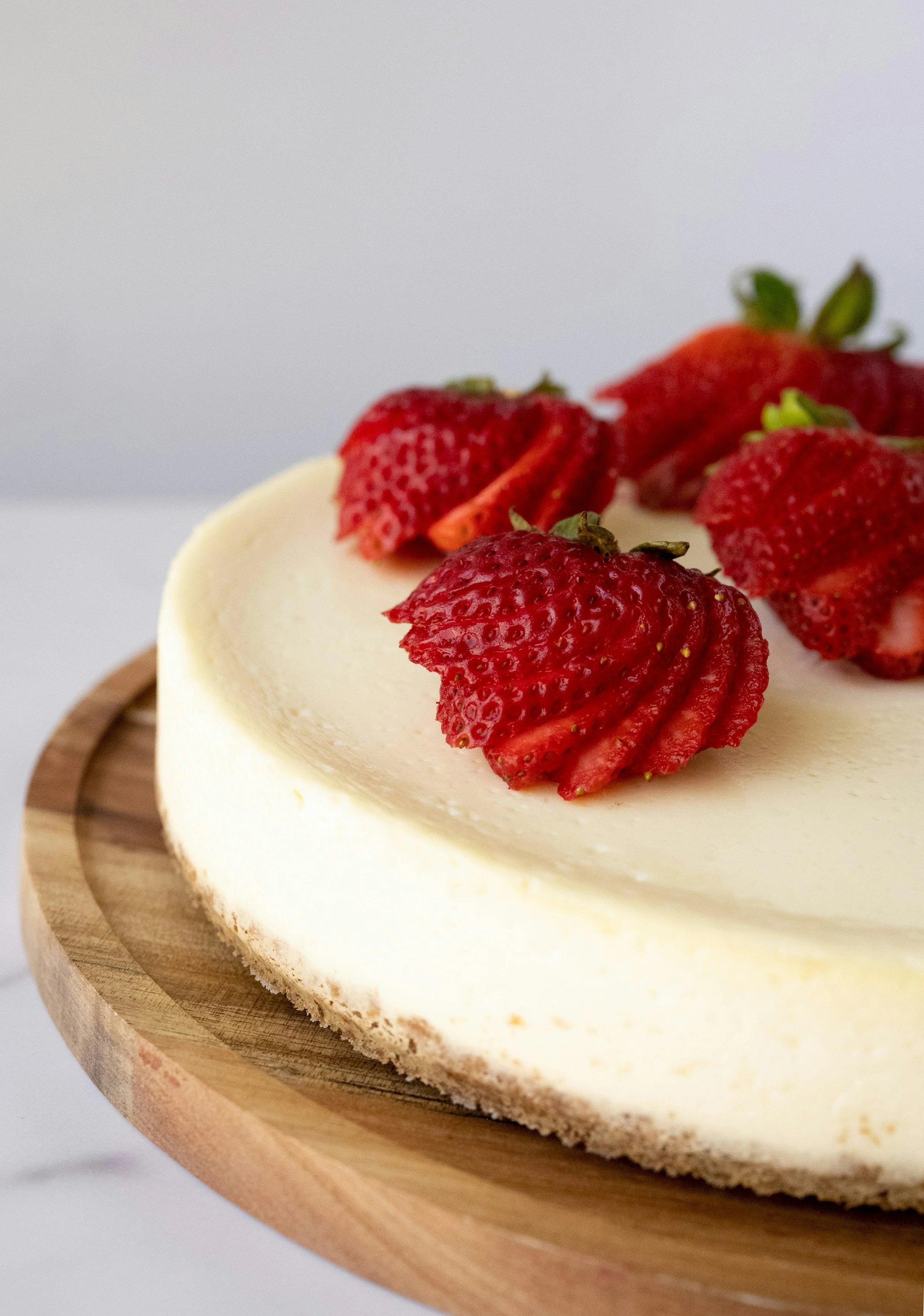 Cheesecake topped with sliced strawberries, on a wooden serving board.