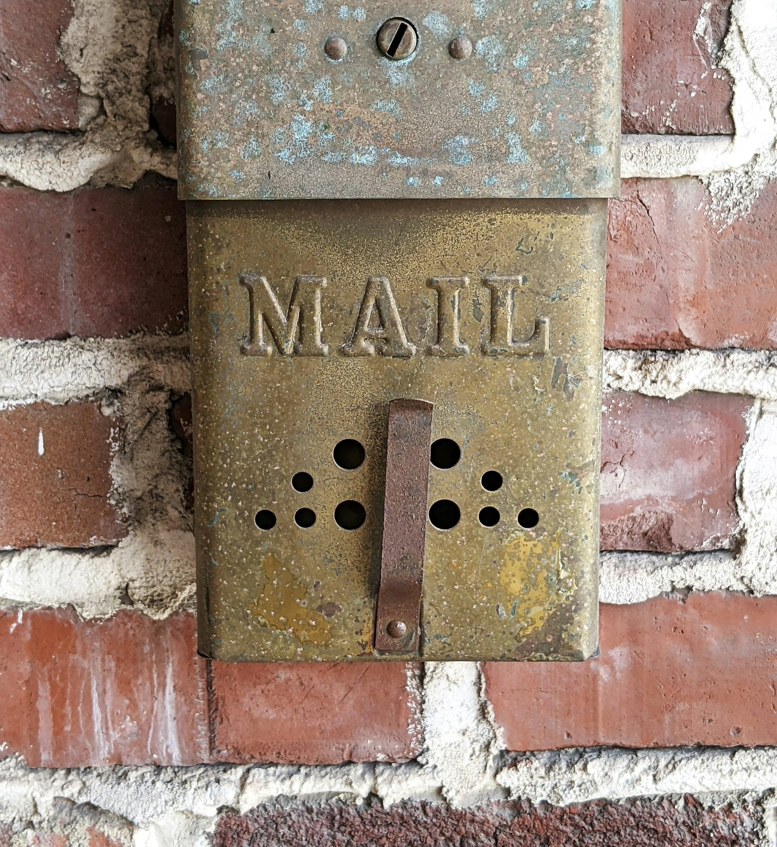 An old, rusty mail collection box mounted on a brick wall.