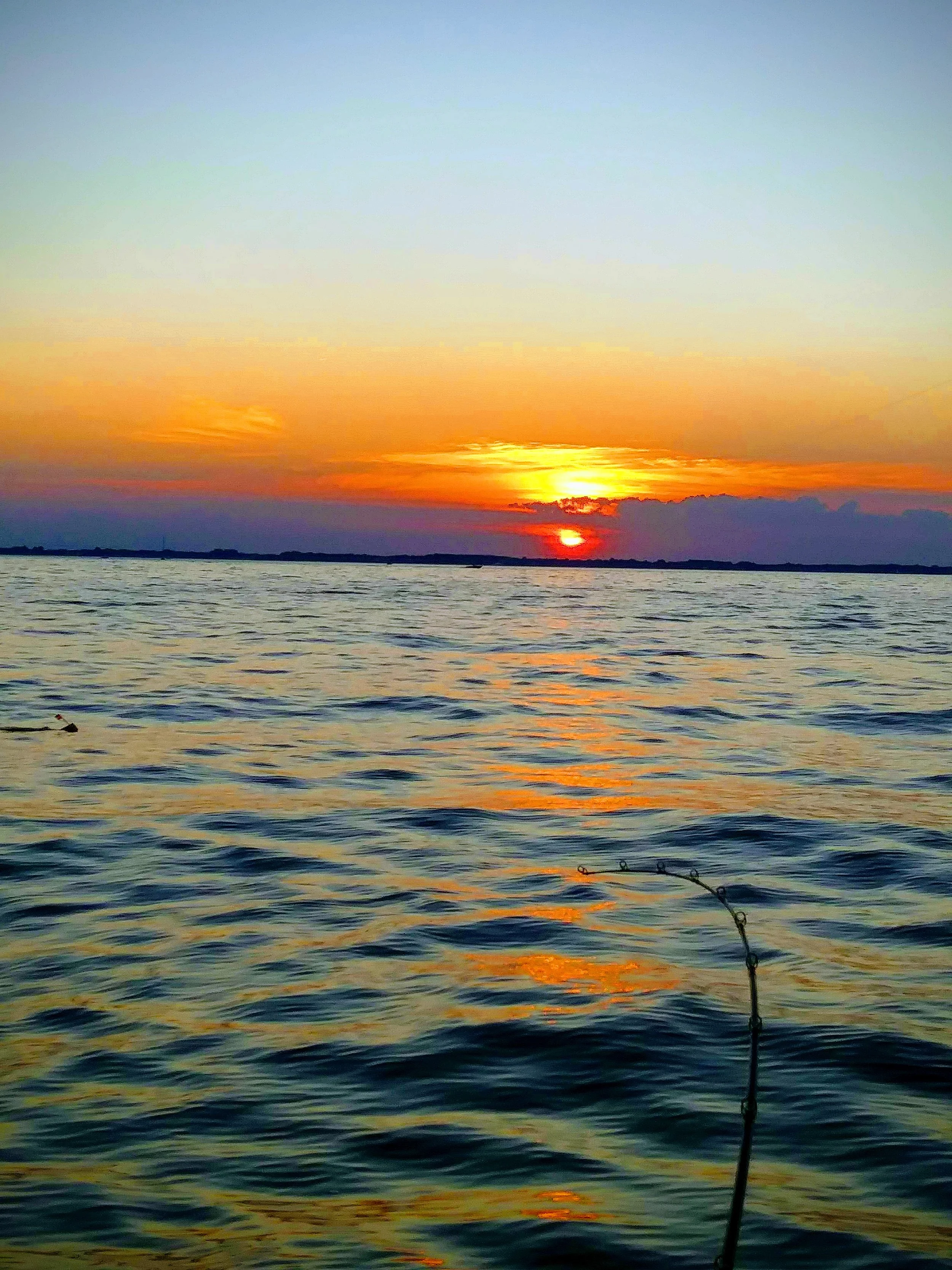 A sunset over a body of water with calm waves, featuring a fishing line in the lower right corner.
