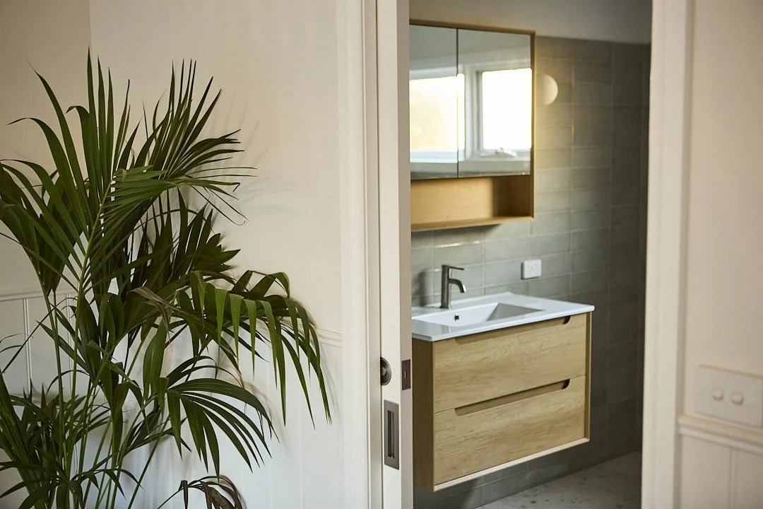 Modern bathroom with wood vanity, white sink, gray tile backsplash, mirrored cabinet, and indoor palm plant