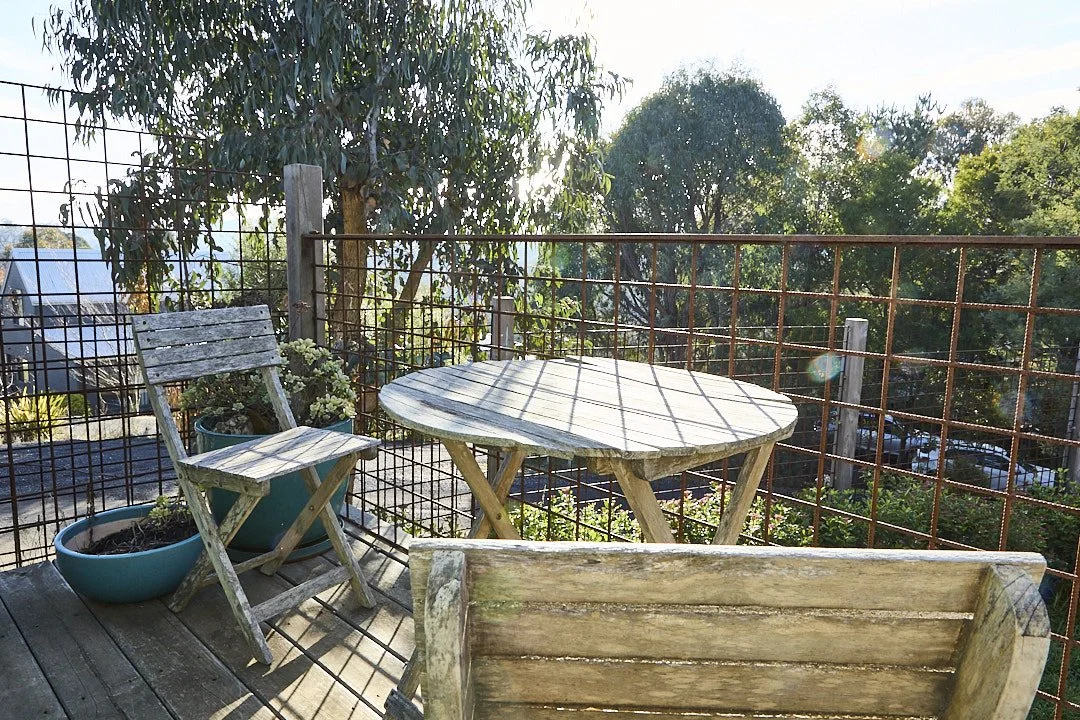 Weathered wooden patio table and chairs on a sunny deck overlooking trees