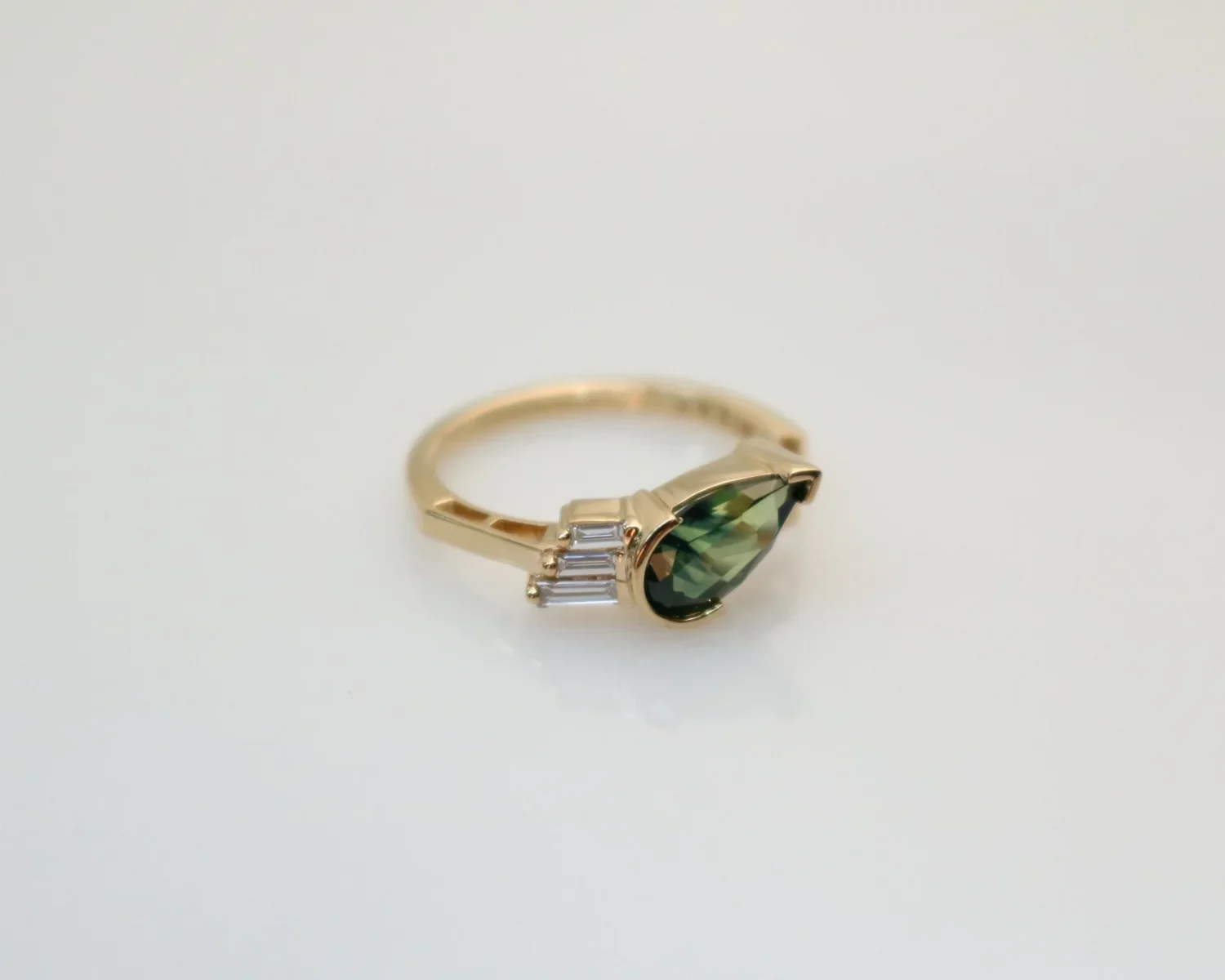 Gold ring with a large faceted green gemstone and small rectangular clear stones on the sides