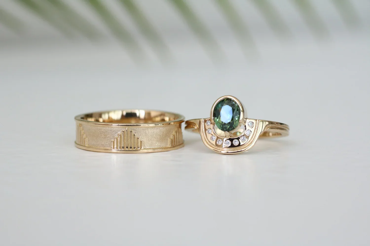 Gold wedding band with engraved geometric pattern and a gold engagement ring with a large oval green gemstone and small diamonds.