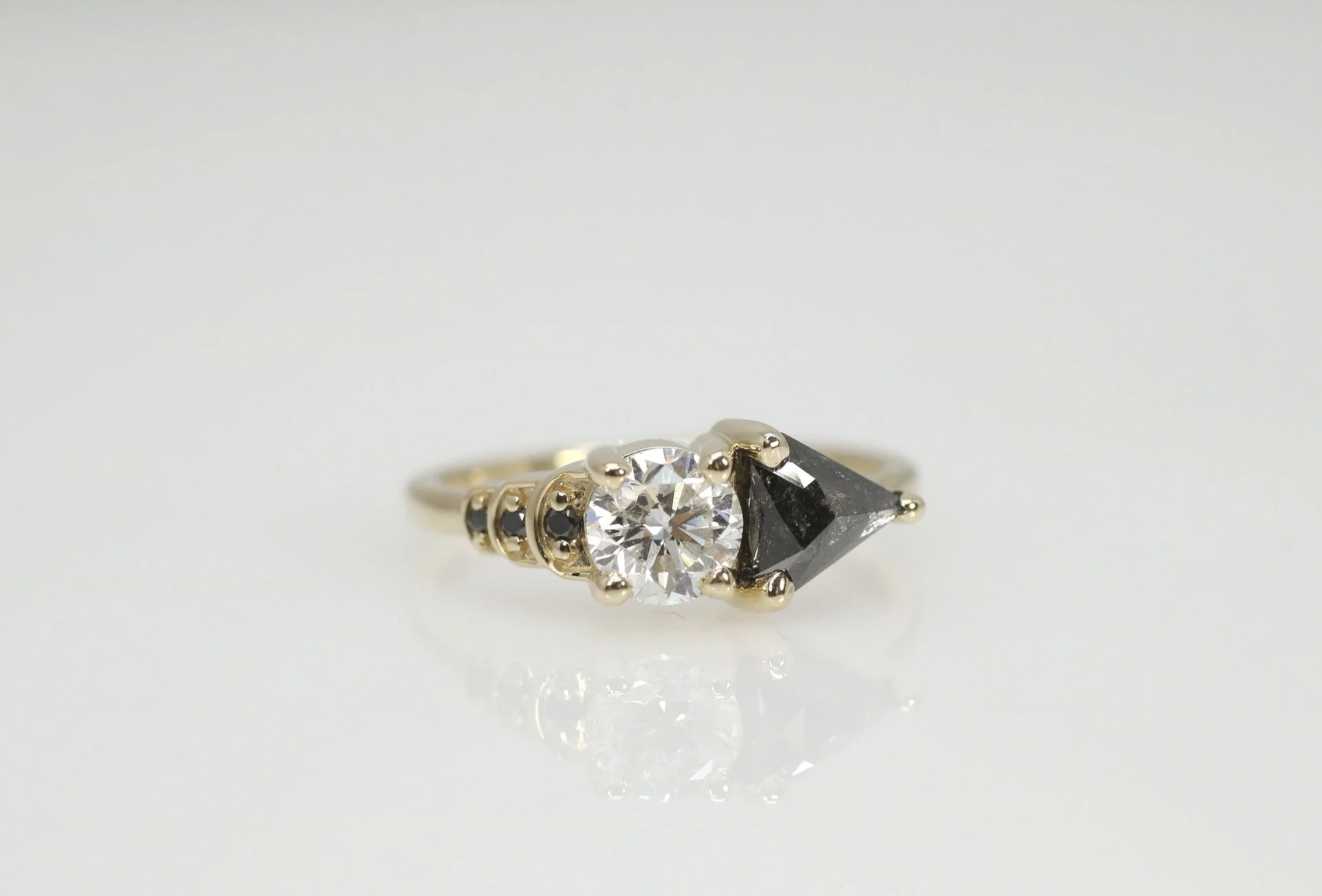 Gold ring with a large round diamond and black triangle-shaped gemstone on a white background.