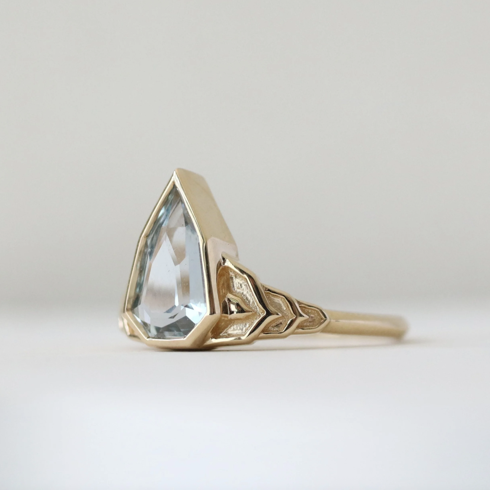 Gold ring with geometric design and large clear gemstone on a white background.